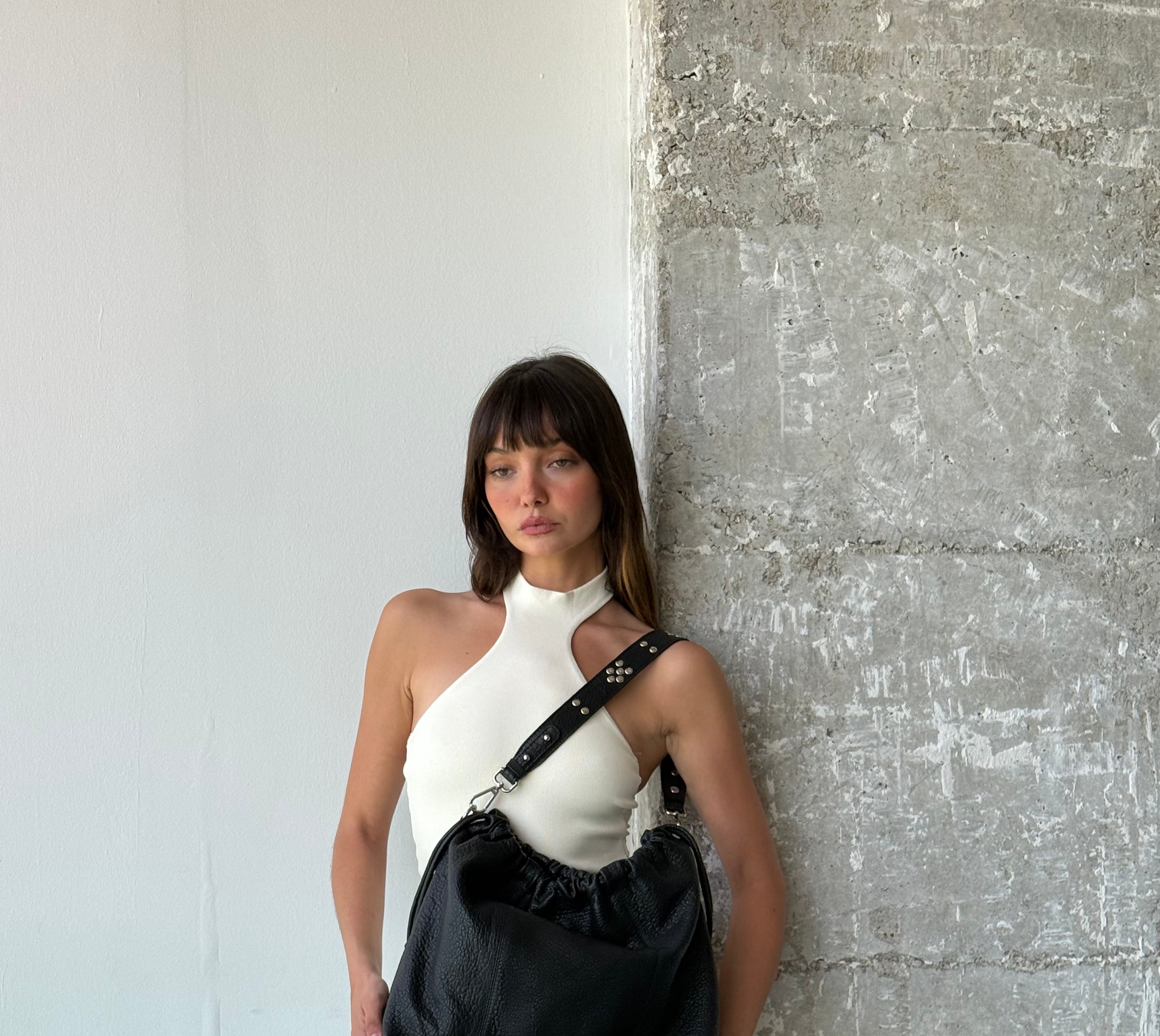Person holding a black leather Neuville bag against a textured wall.