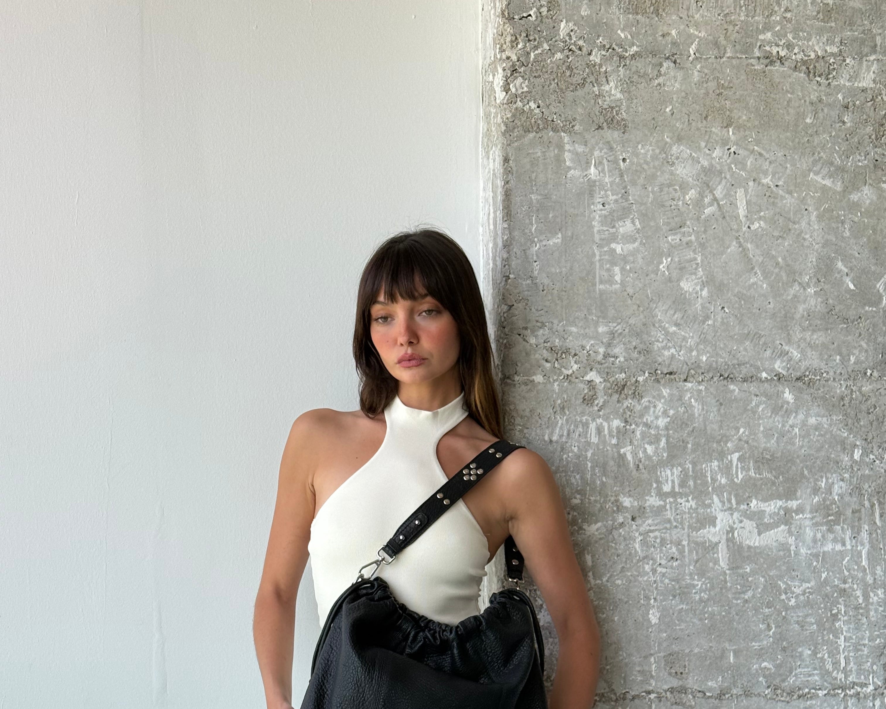 Person holding a black leather Neuville bag  against a textured wall.