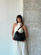 Person holding a black leather Neuville bag  against a textured wall.
