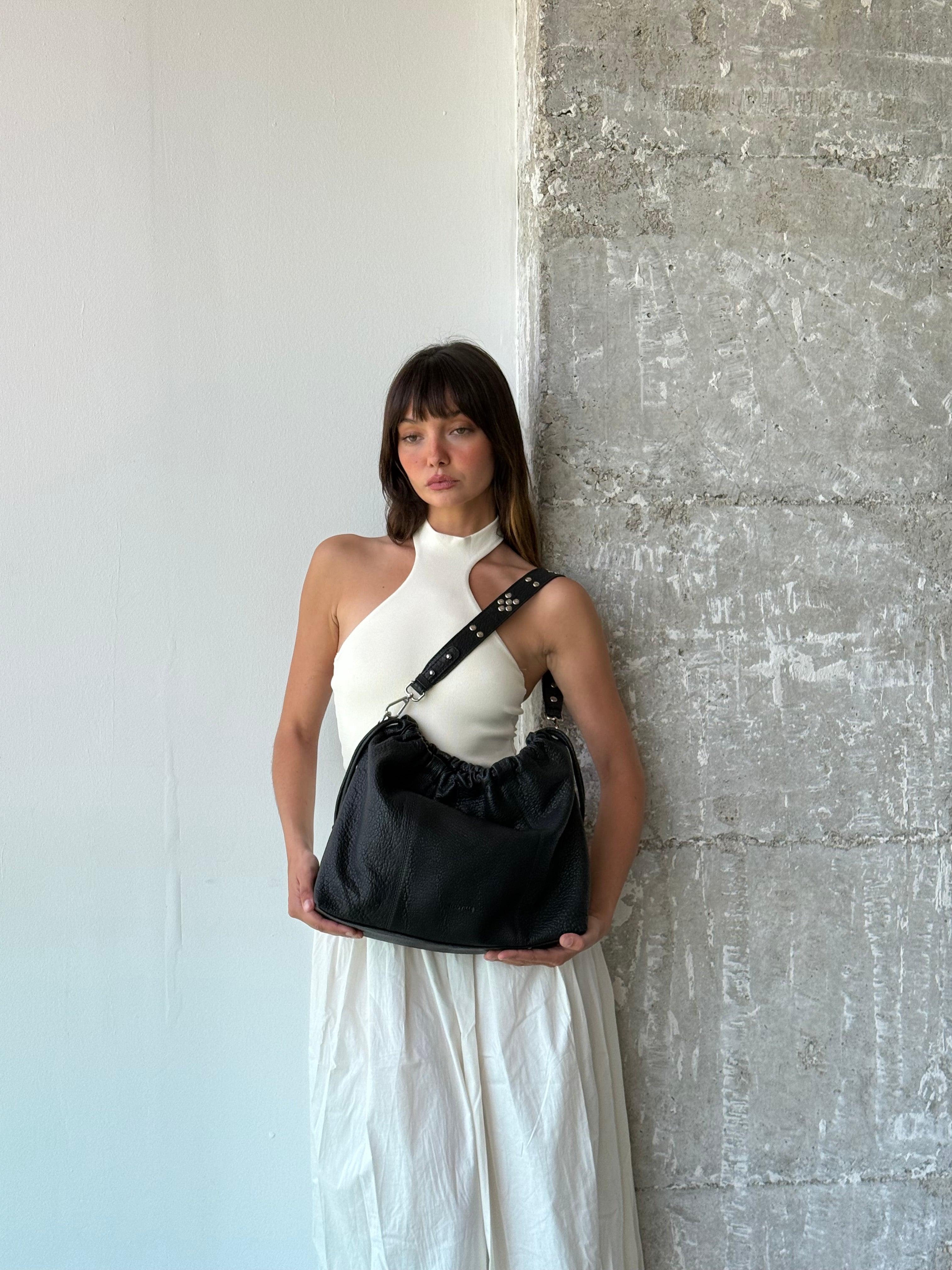 Person holding a black leather Neuville bag  against a textured wall.