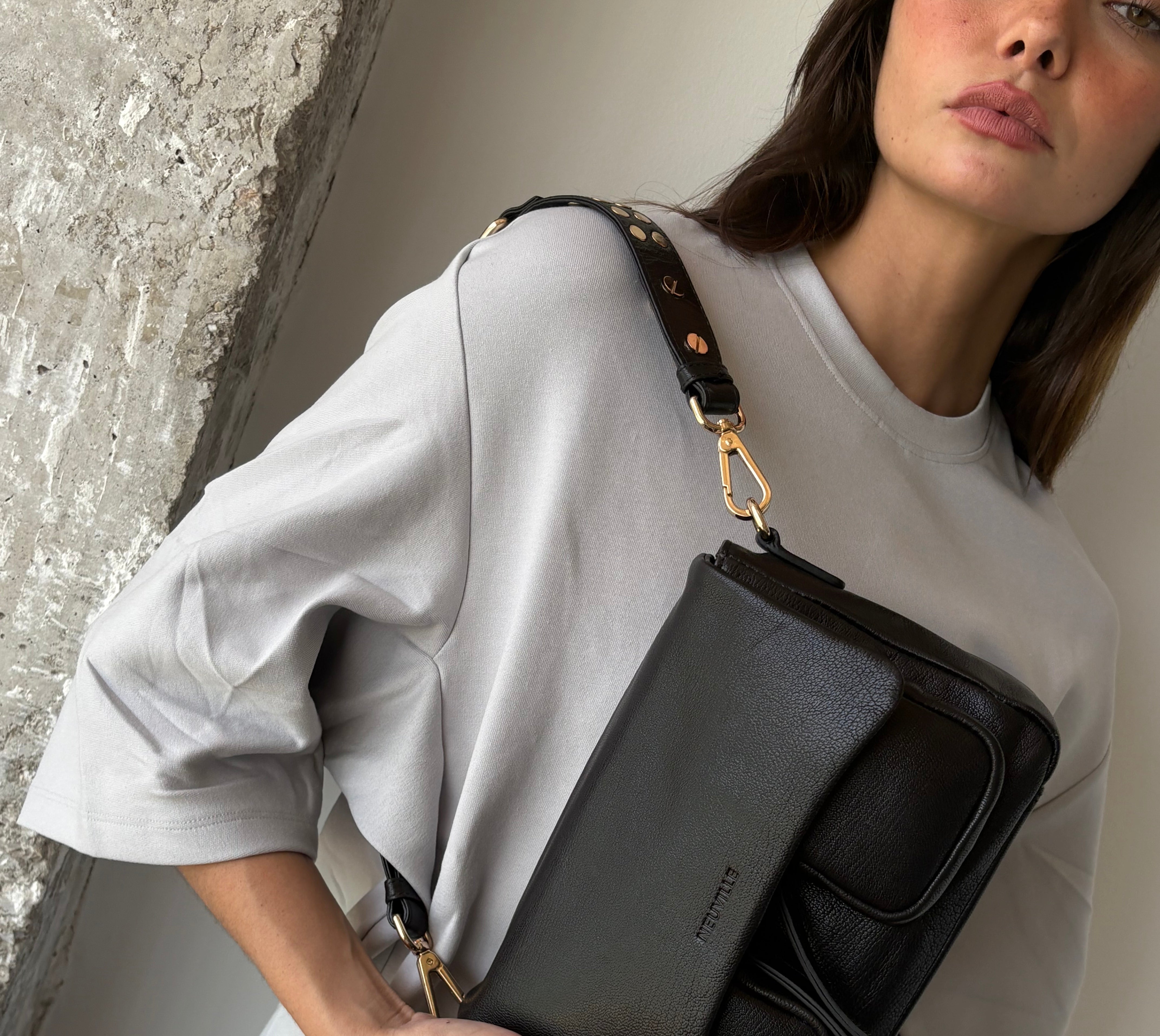 Woman holding a black handbag with a visible brand logo.