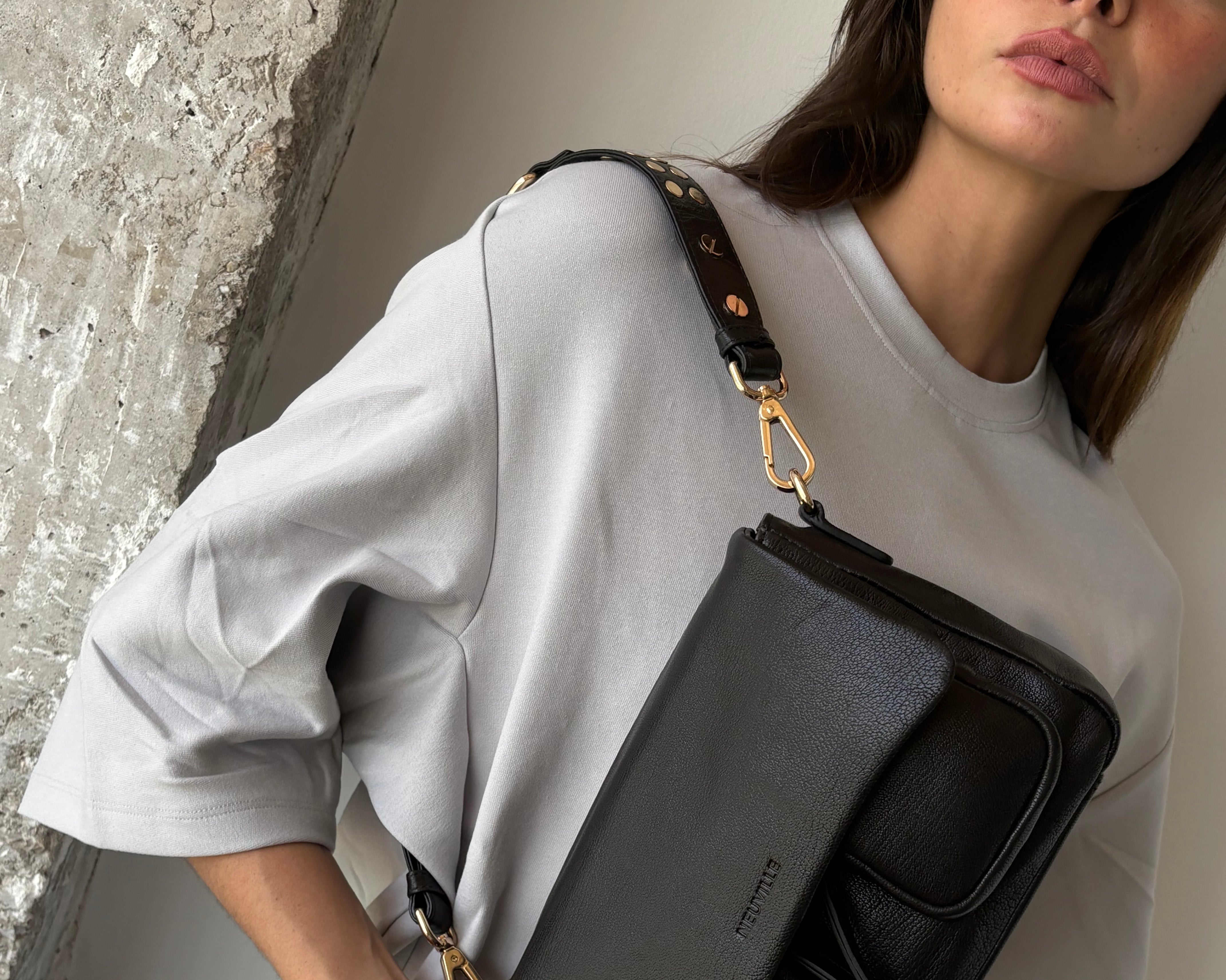 Woman holding a black handbag with a visible brand logo.