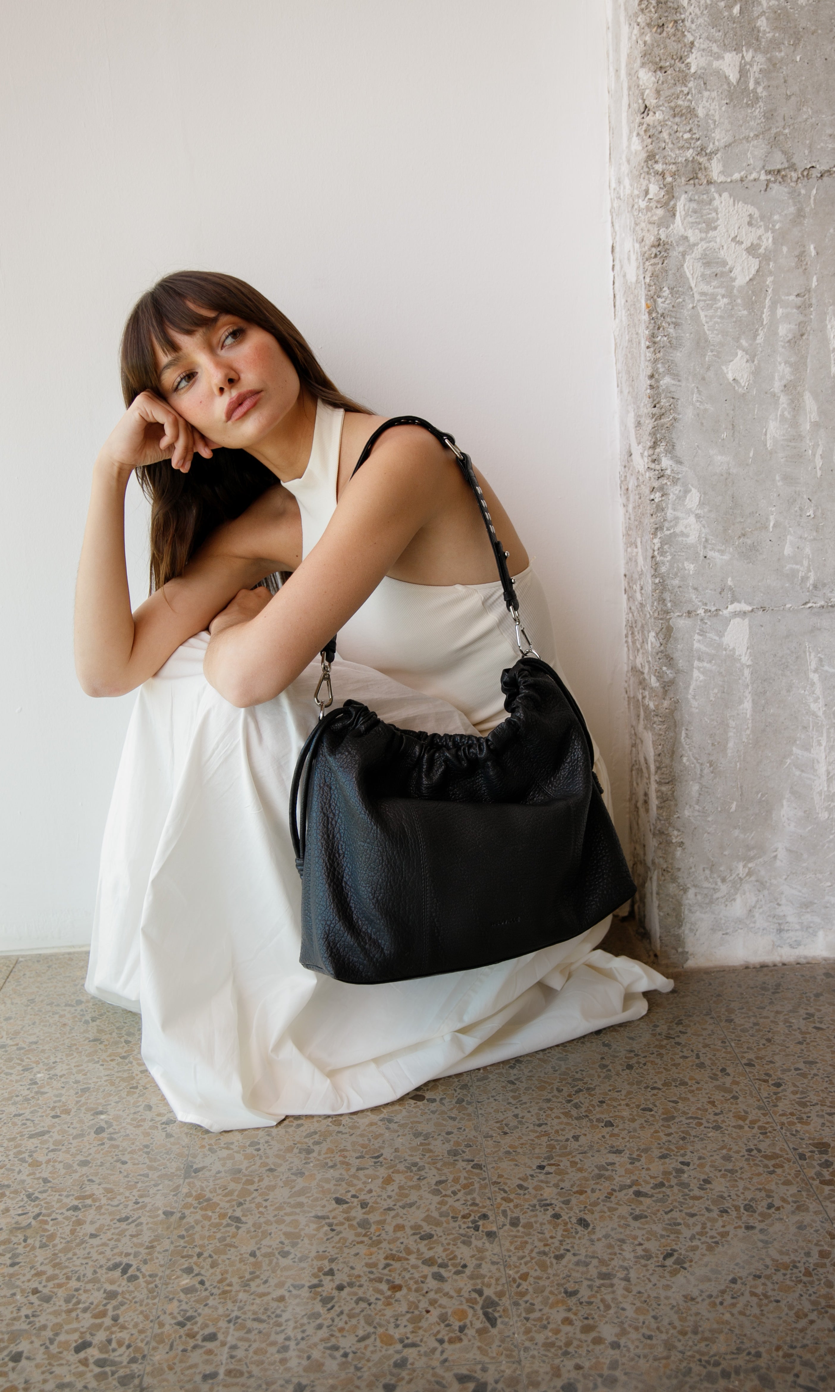 Woman holding a black Elliot Neuville handbag against a white wall.