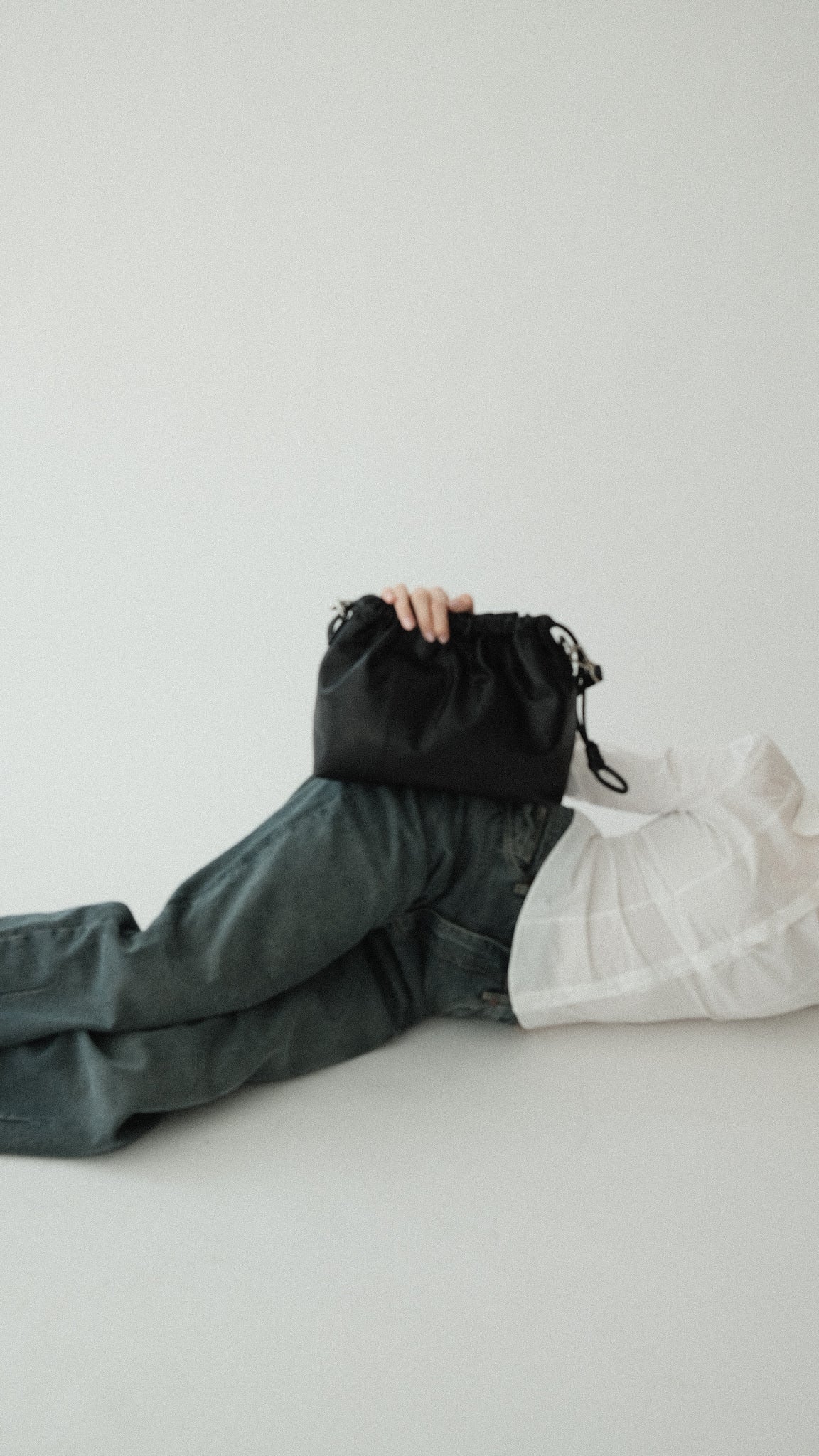 A small black Elliot leather handbag with a shoulder strap, displayed on a person lying down.