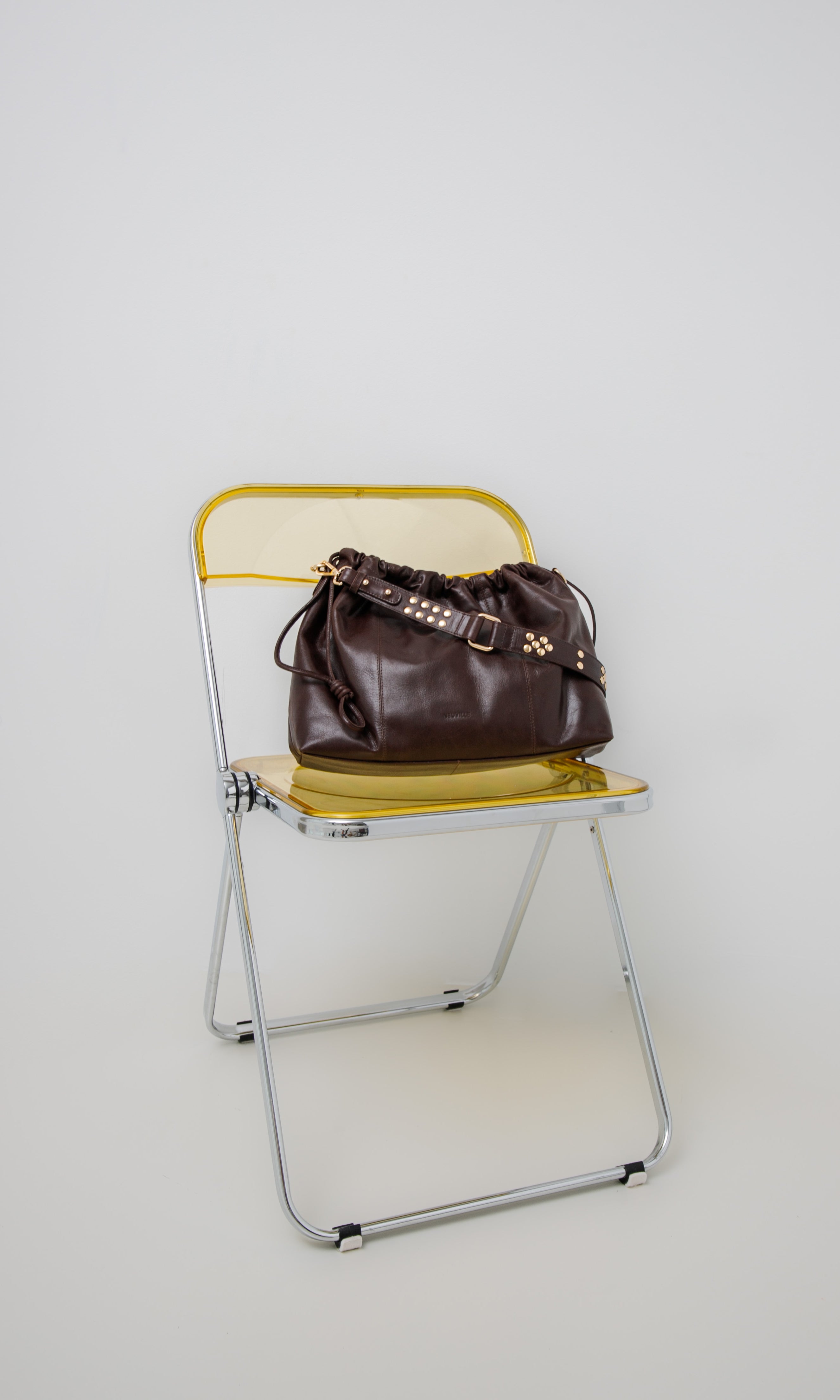 Elliot Chocolate (gold) Brown leather handbag on a yellow folding chair against a white background
