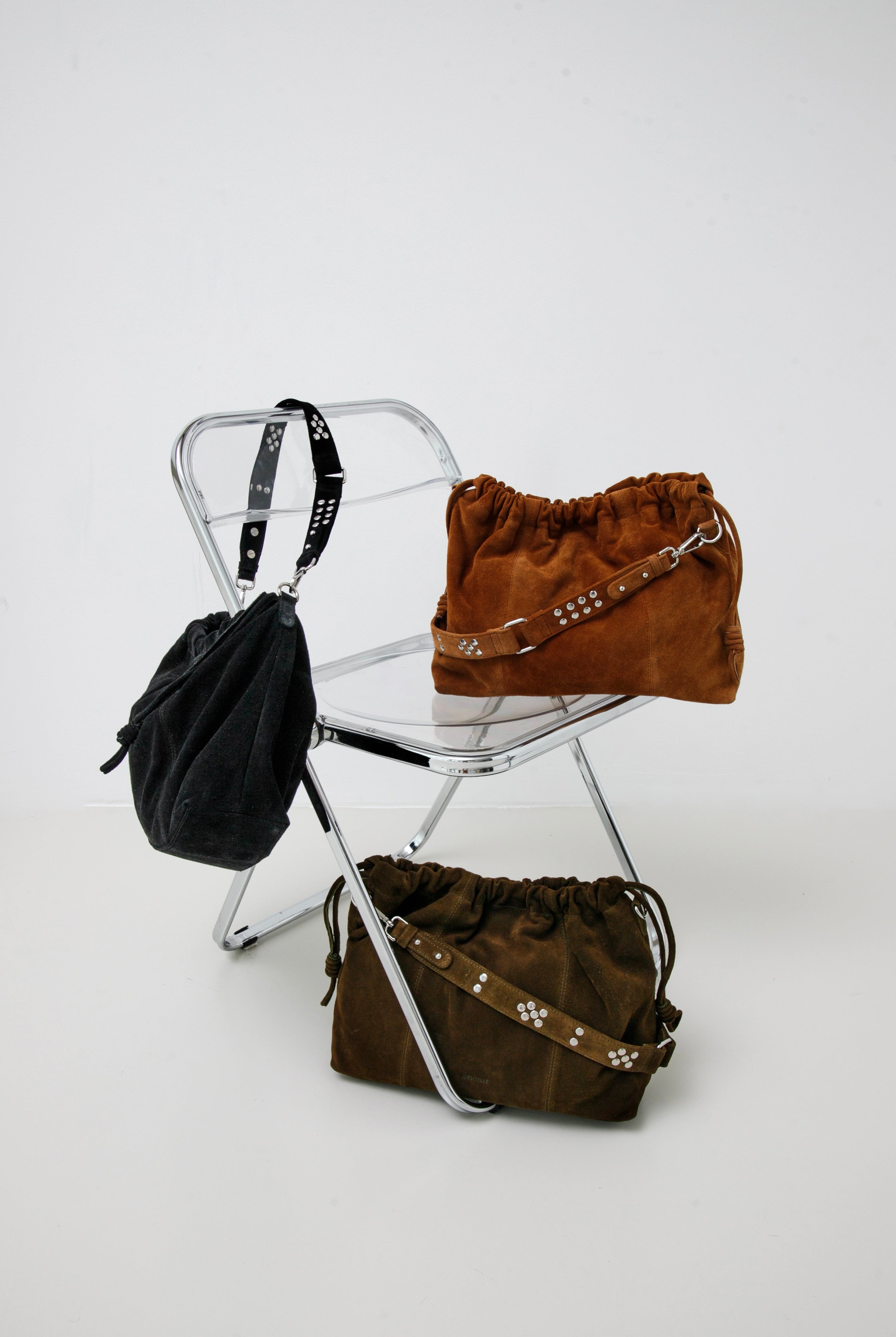 Elliot Black suede, Elliot Caremel suede and Elliot khaki suede bags on a white chair against a white background: Neuville leather bags.