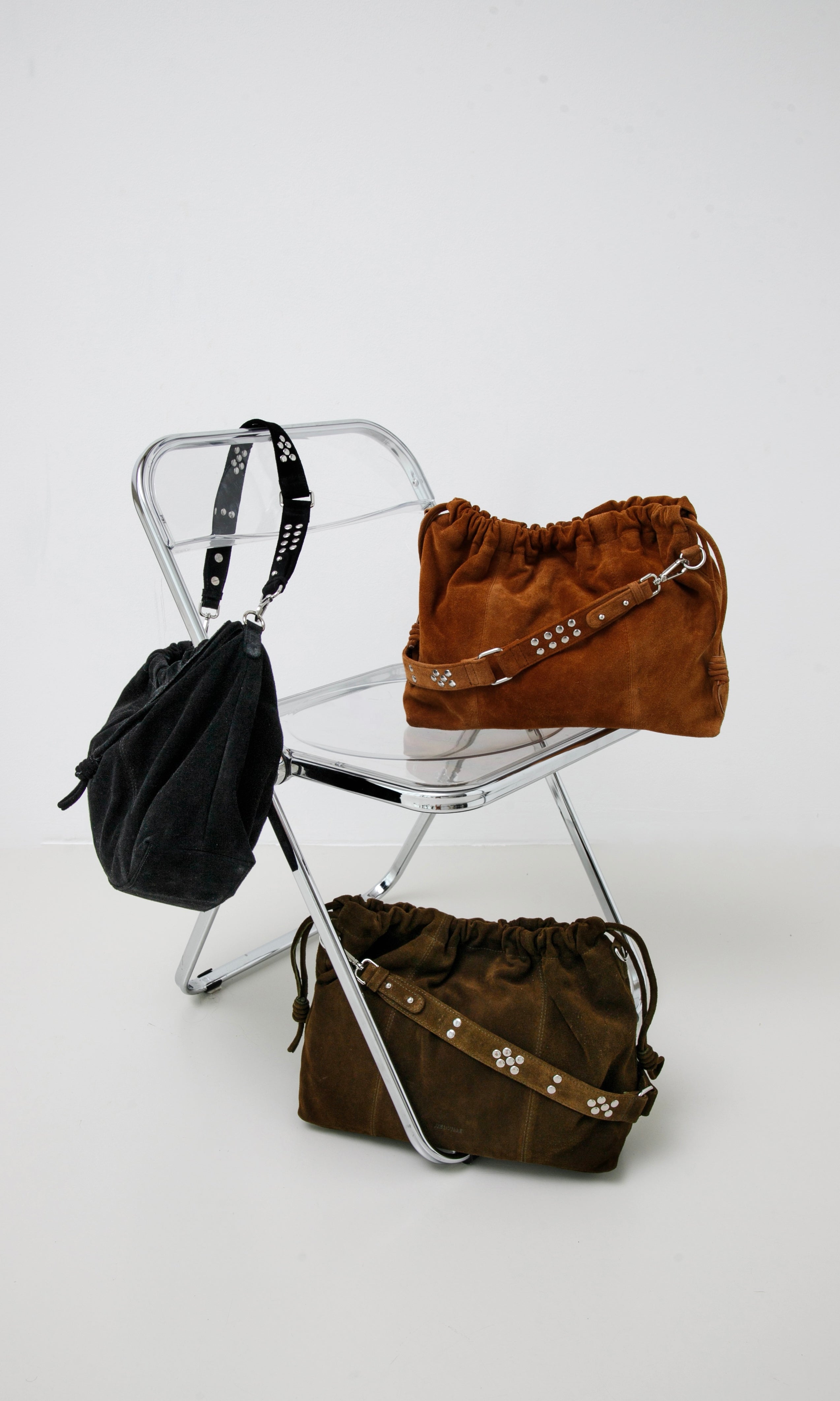 Elliot Black suede, Elliot Caremel suede and Elliot khaki suede bags  on a white chair against a white background: Neuville leather bags.