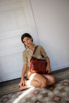 Woman sitting on a patterned floor holding Elliot bag in Burgundy of the brand Neuville.