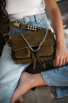 Maxke Suede Khaki  bag with chain detail held by a person wearing light blue jeans.