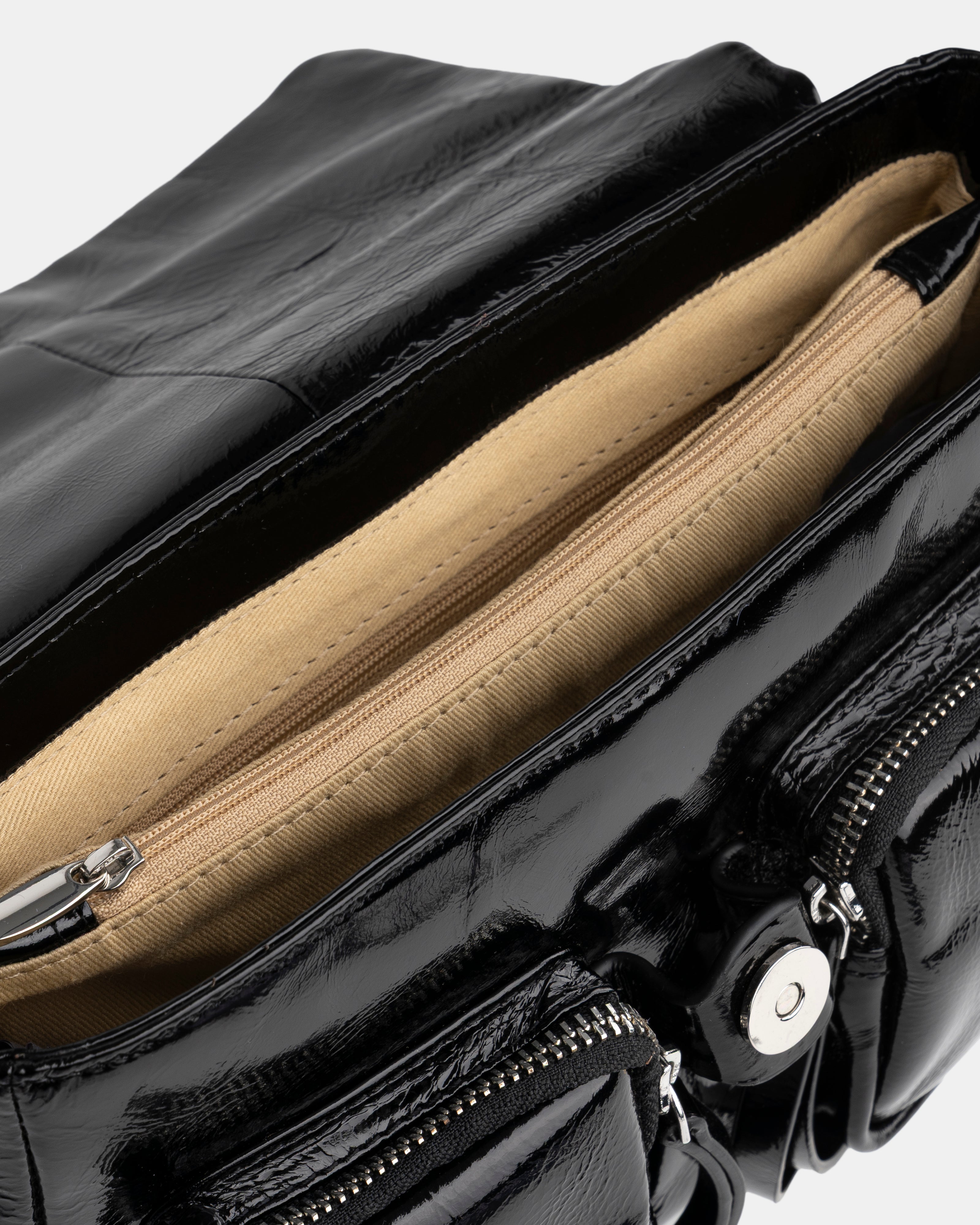 Close-up of a black patent leather handbag with beige interior lining.