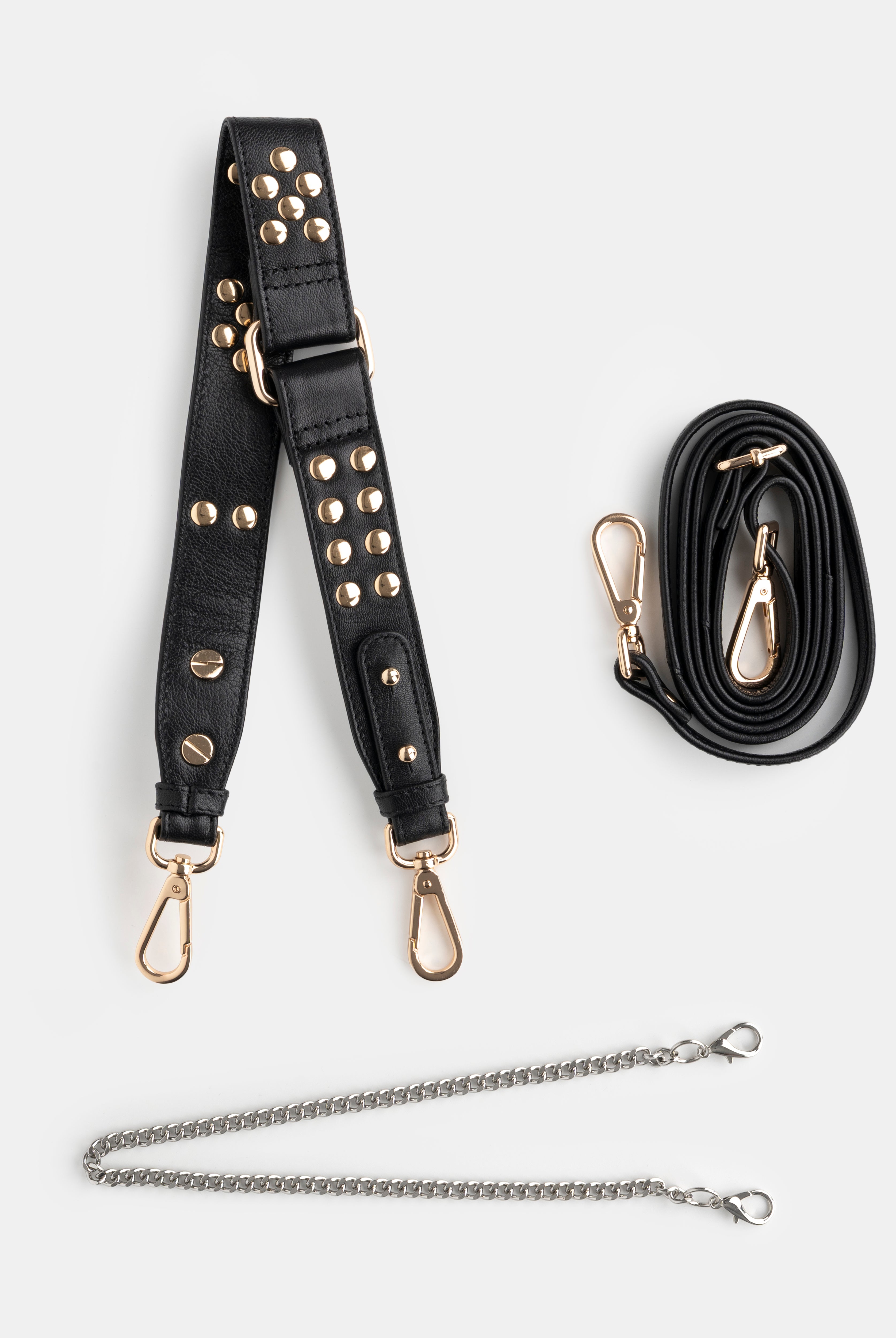 Black studded shoulder bag strap with gold hardware and a black crossbody strap and a golden chain on a white background
