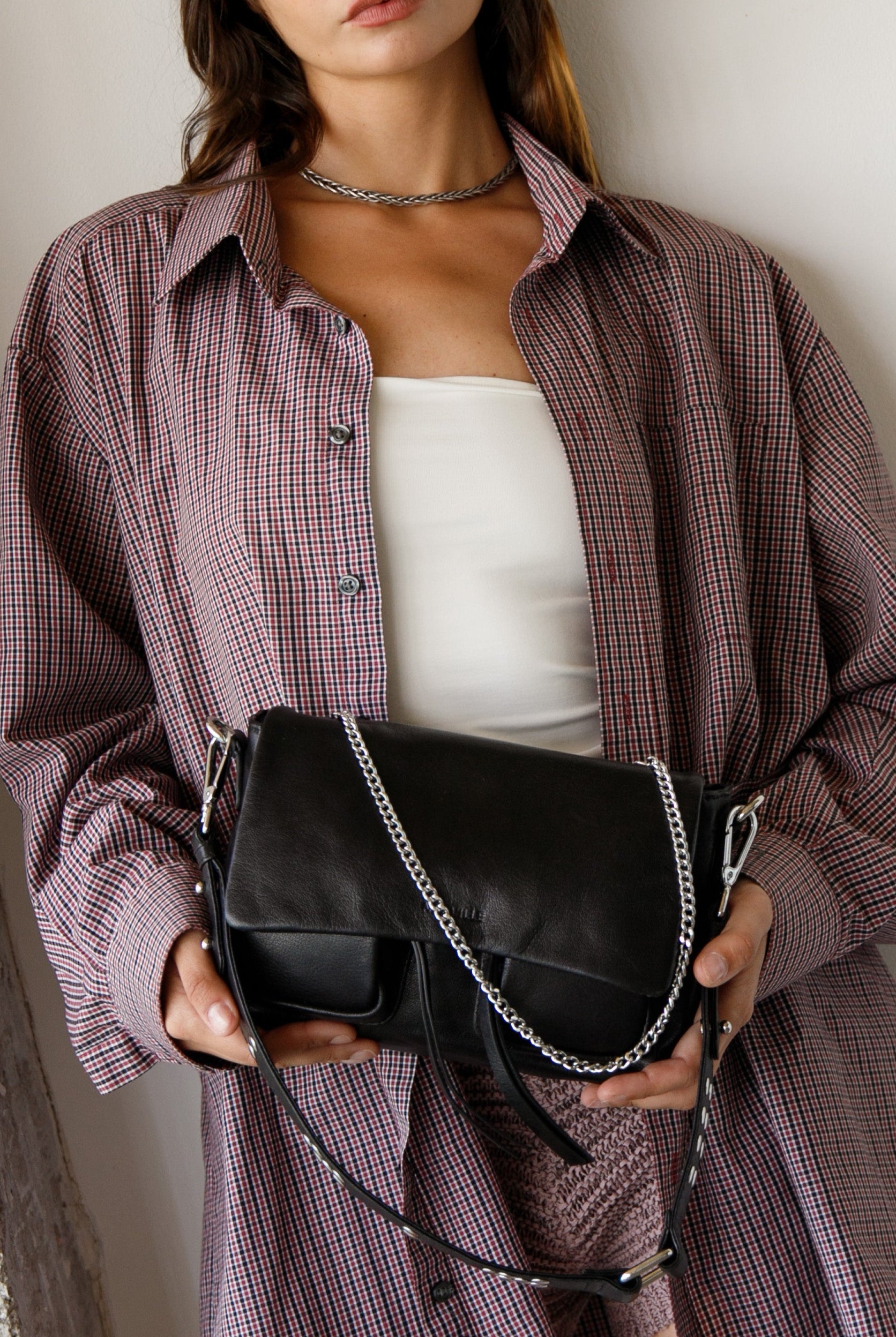 Person wearing a plaid shirt holding a black leather Maxke Black handbag
