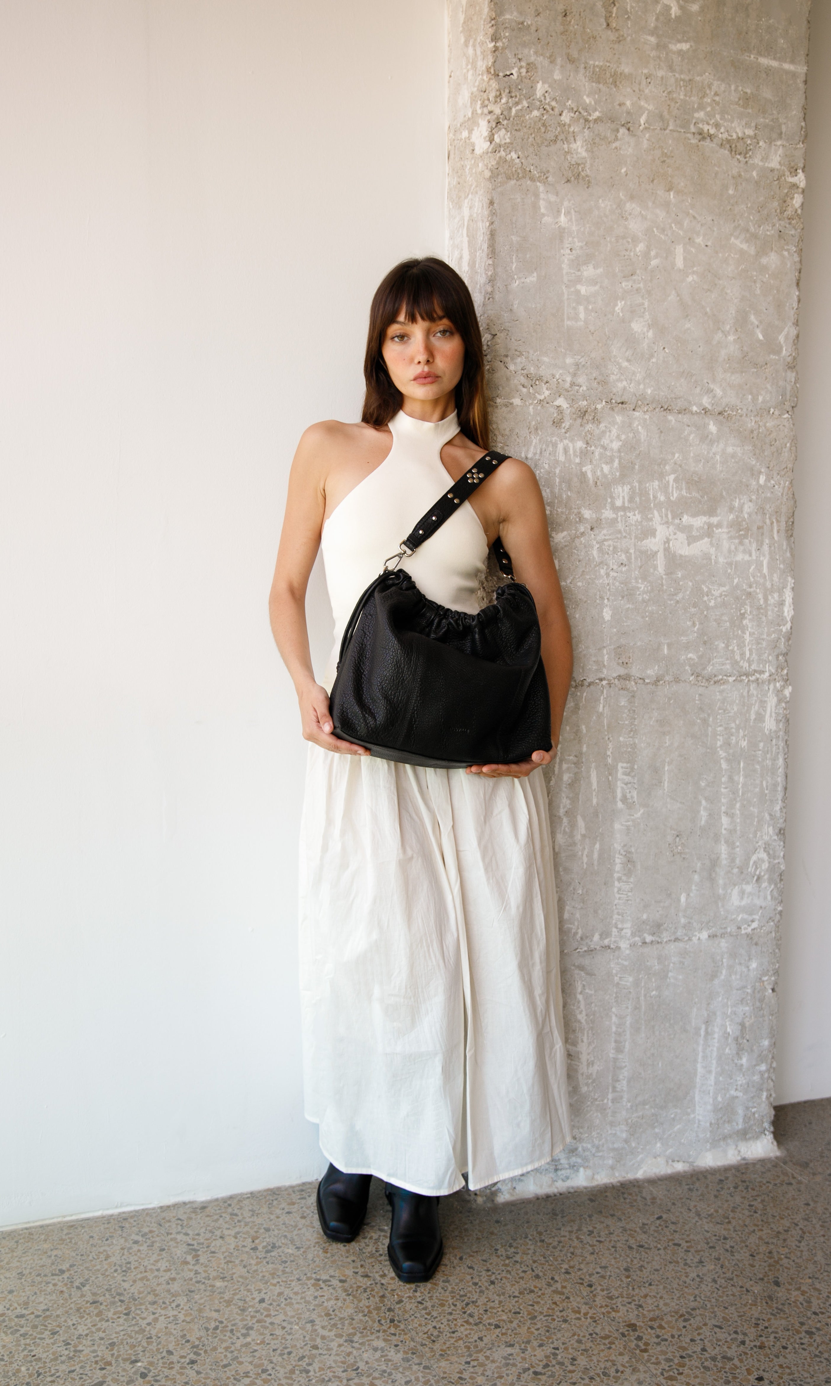 Woman in a white dress holding Bubble black Elliot Neuville bag against a textured wall.