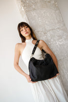 Woman holding Elliot Bubble Black  handbag of the brand Neuville against a textured white wall