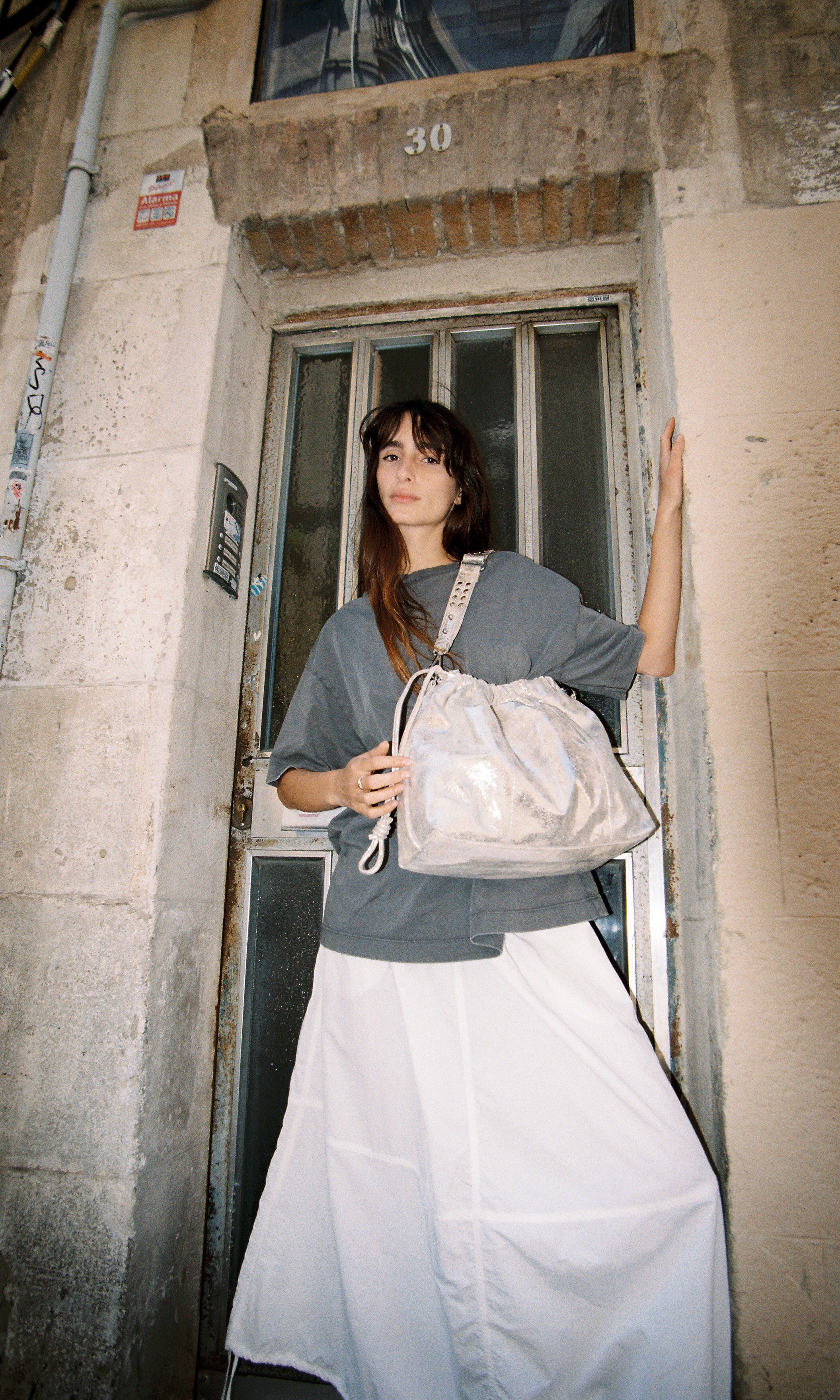 Model wearing Elliot Sand gold shoulderbag and crossbody bag of the brand Neuville in front of a door