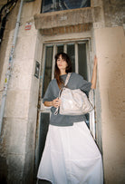 Model wearing Elliot Sand gold shoulderbag and crossbody bag of the brand Neuville in front of a door