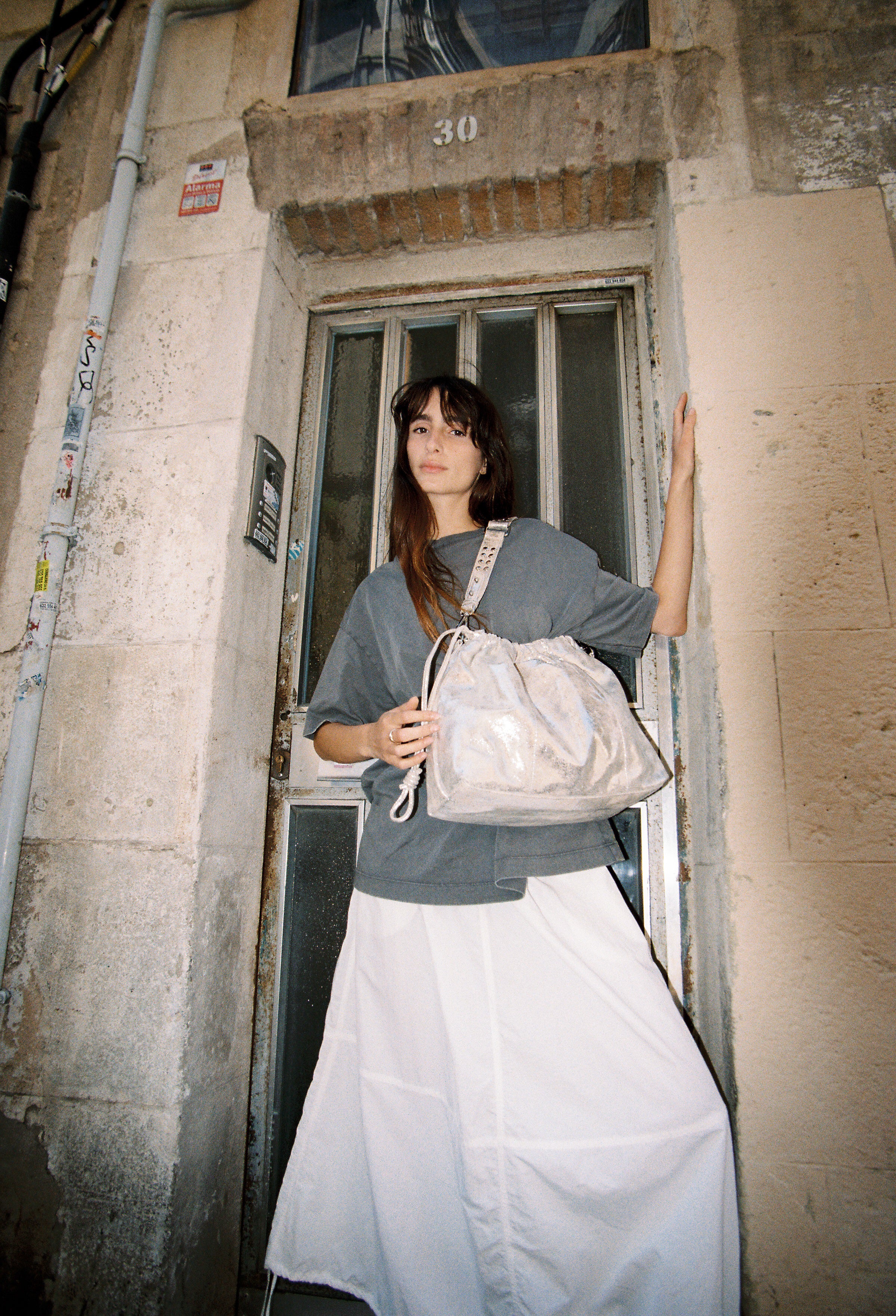 Model wearing Elliot Sand gold shoulderbag and crossbody bag of the brand Neuville in front of a door