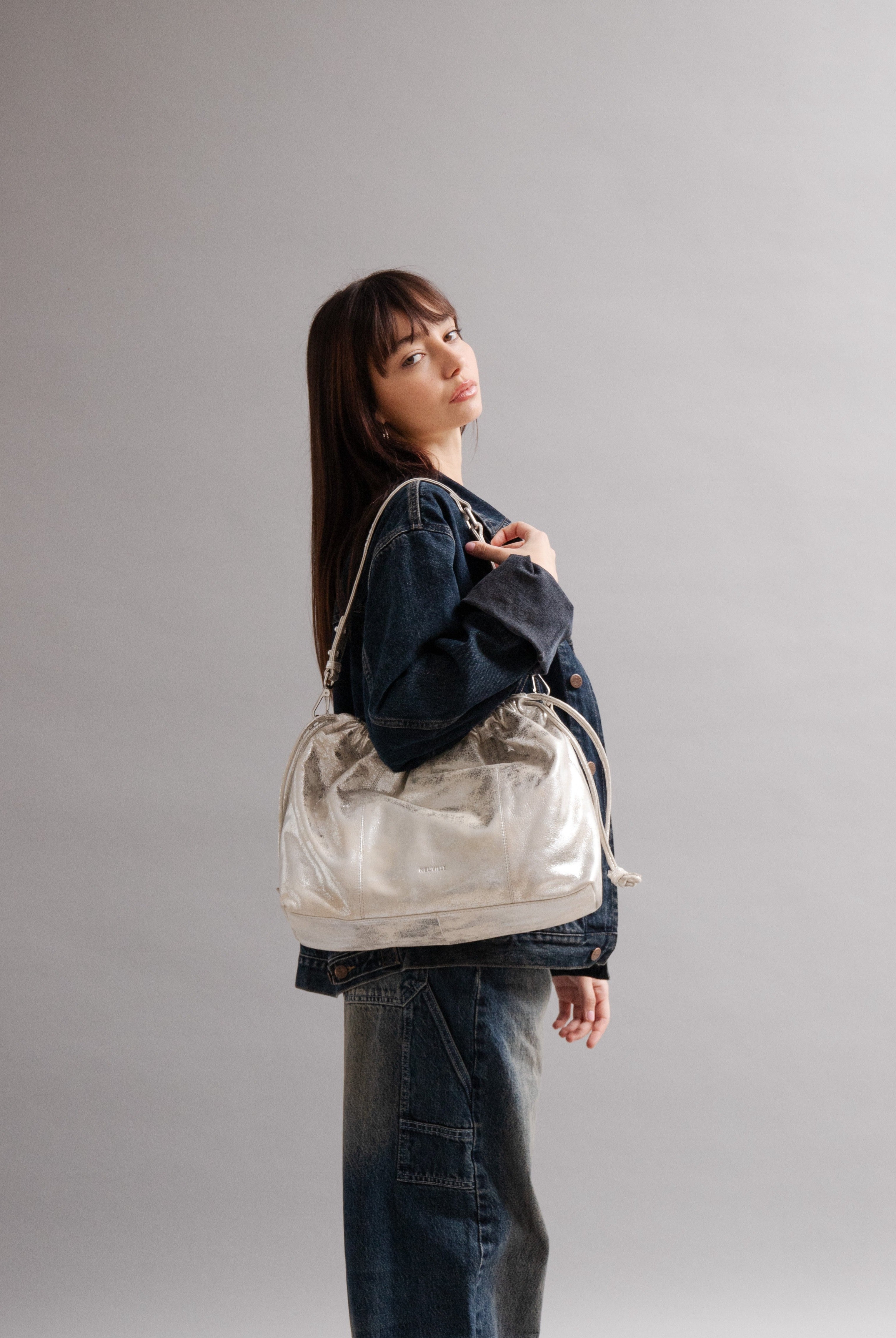 Elliot Sand Gold metallic drawstring bag on a model of in front of a grey background: Neuville bag