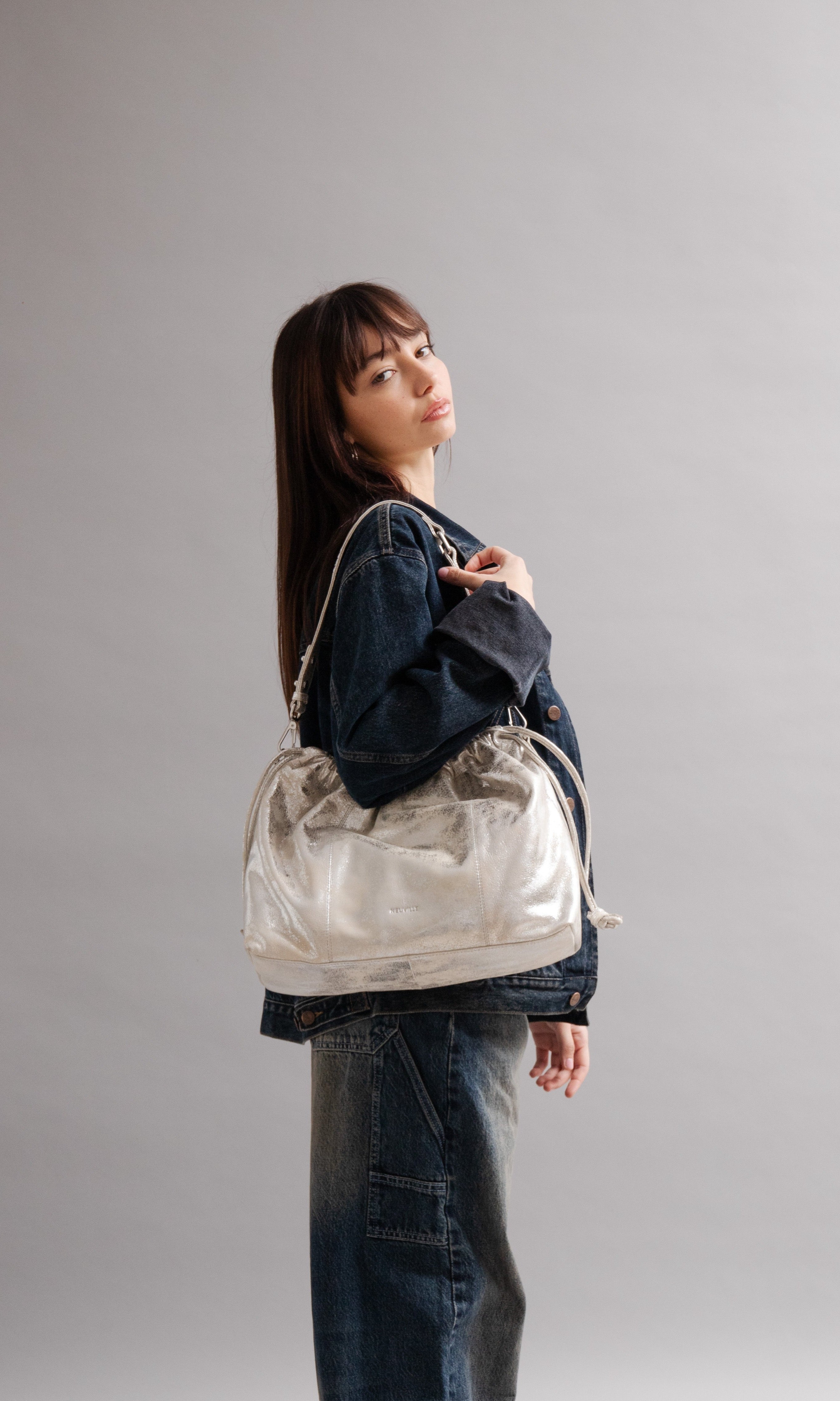 Elliot Sand Gold metallic drawstring bag on a model of in front of a grey background: Neuville bag