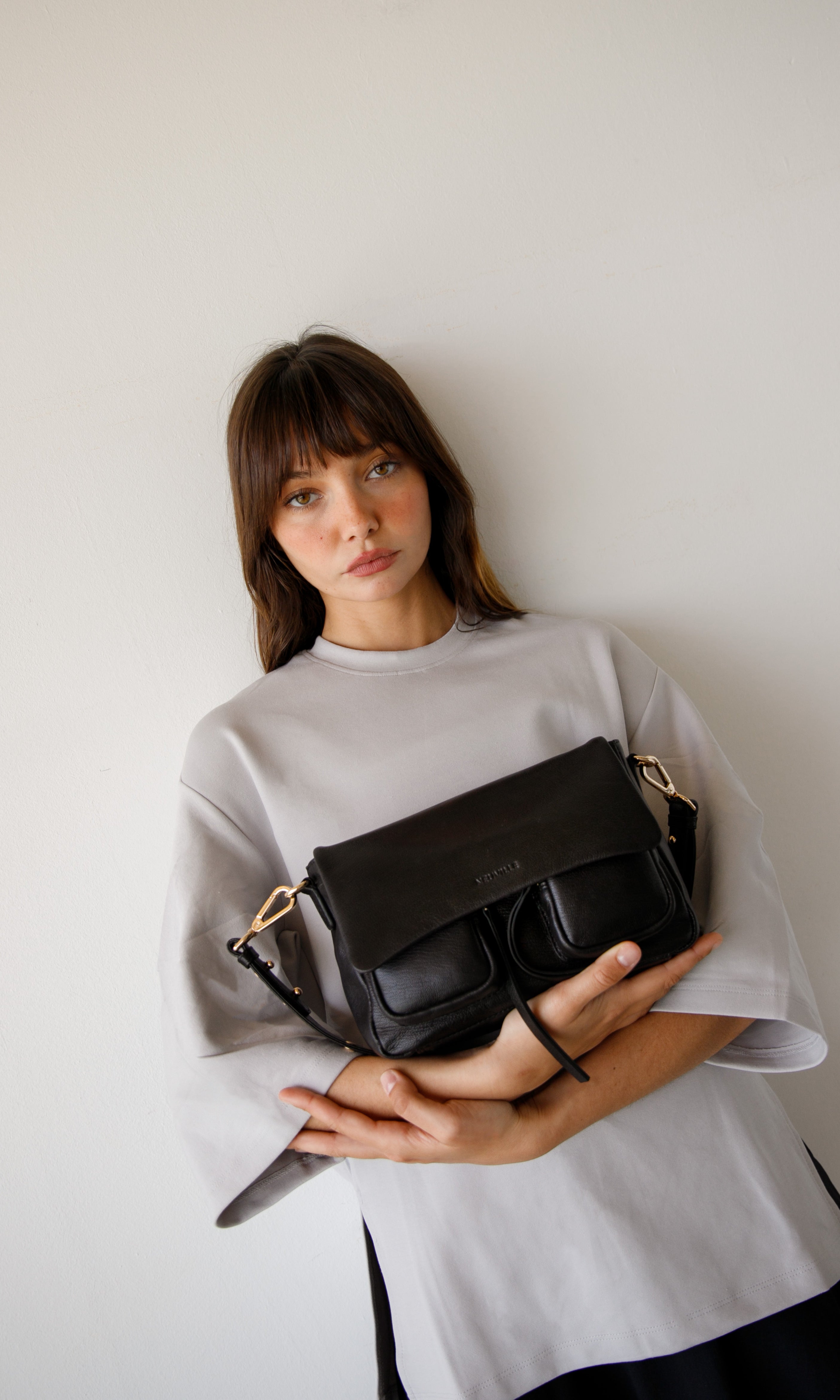 Woman holding a black handbag against a plain background