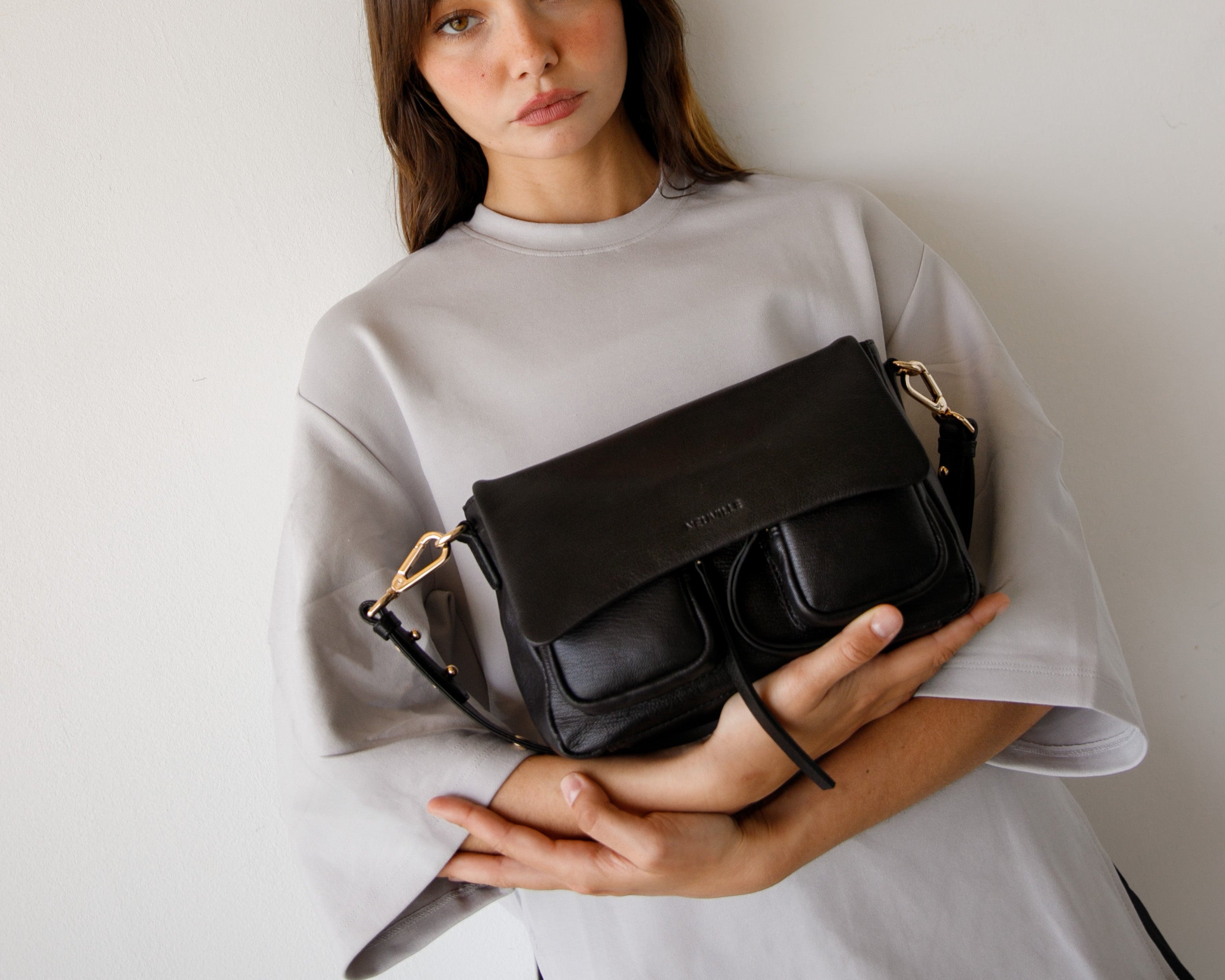 Woman holding a black handbag against a plain background