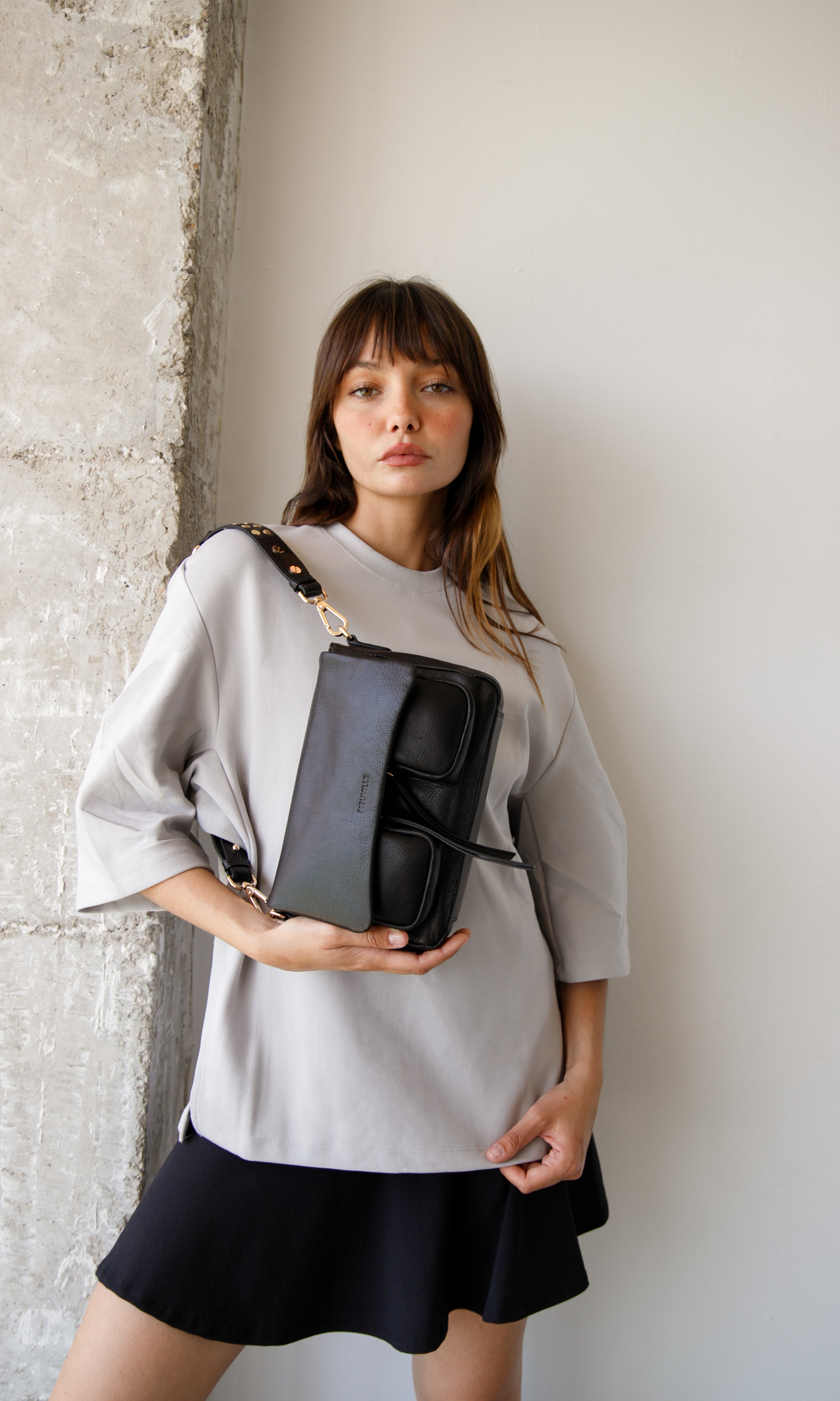 Woman holding a black leather handbag against a neutral background. Maxke Black (gold) Neuville