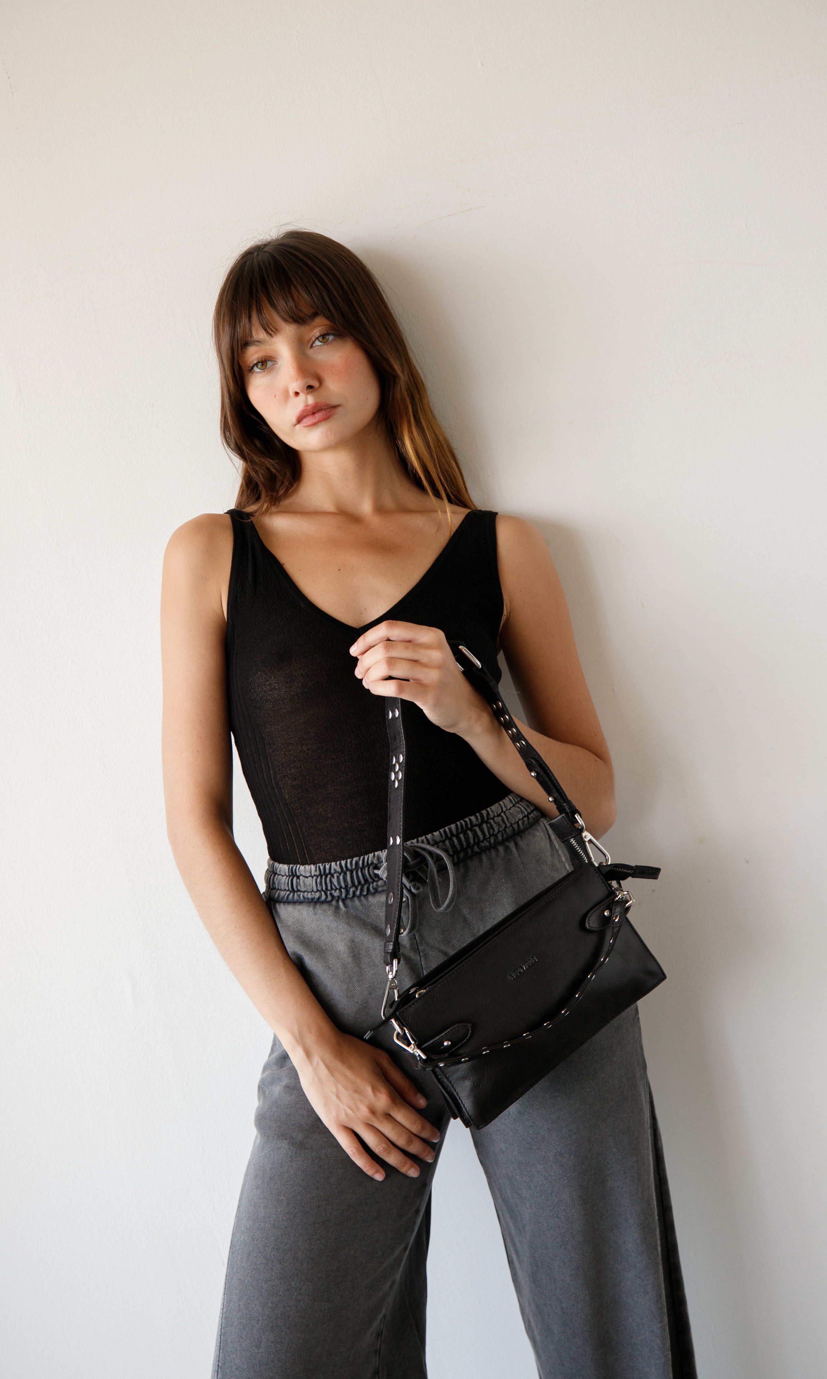 Woman holding a black handbag against a plain background