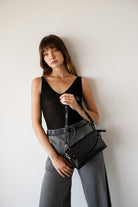 Woman holding a black handbag against a plain background