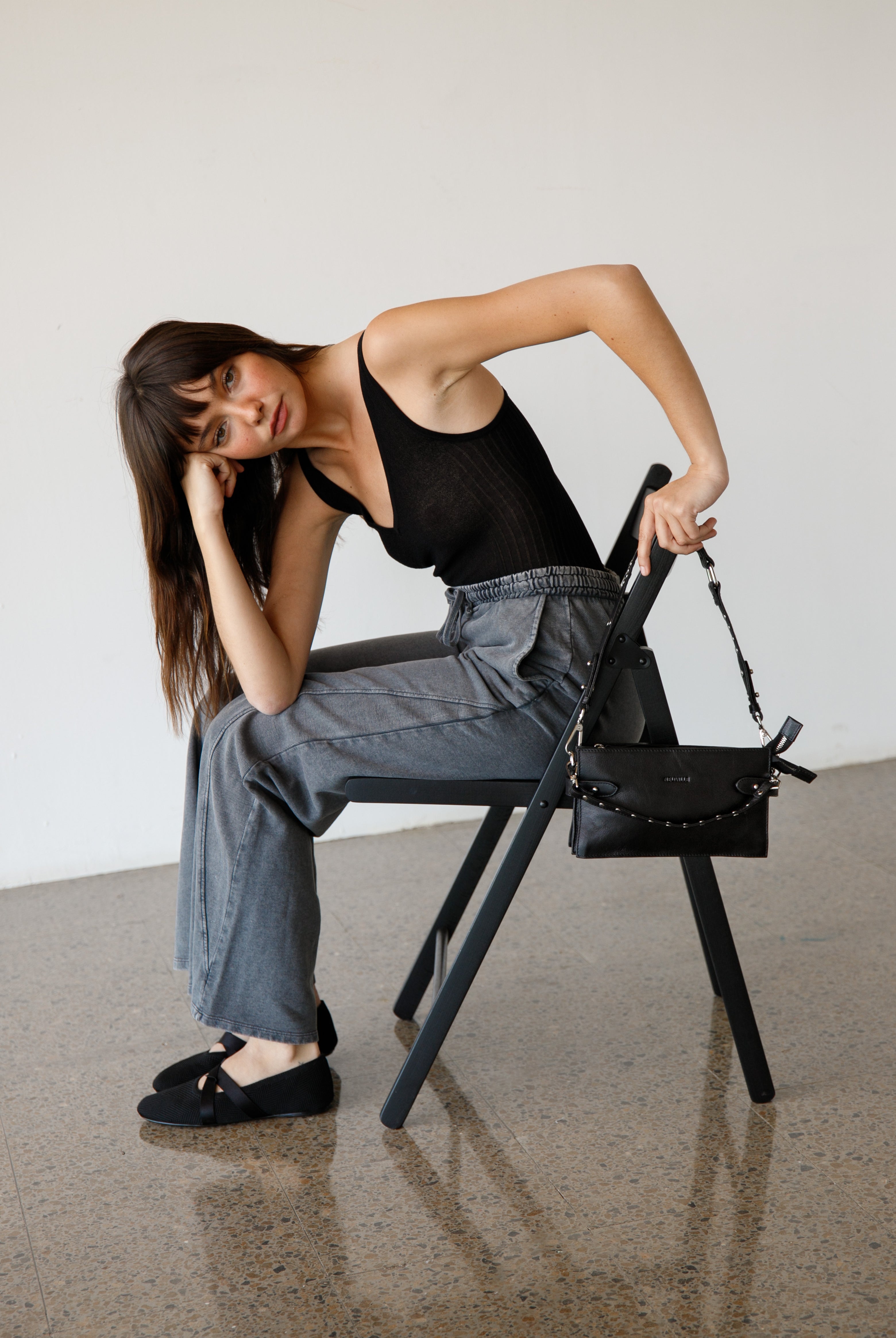 Woman sitting on a chair with a black handbag next to her against a plain background