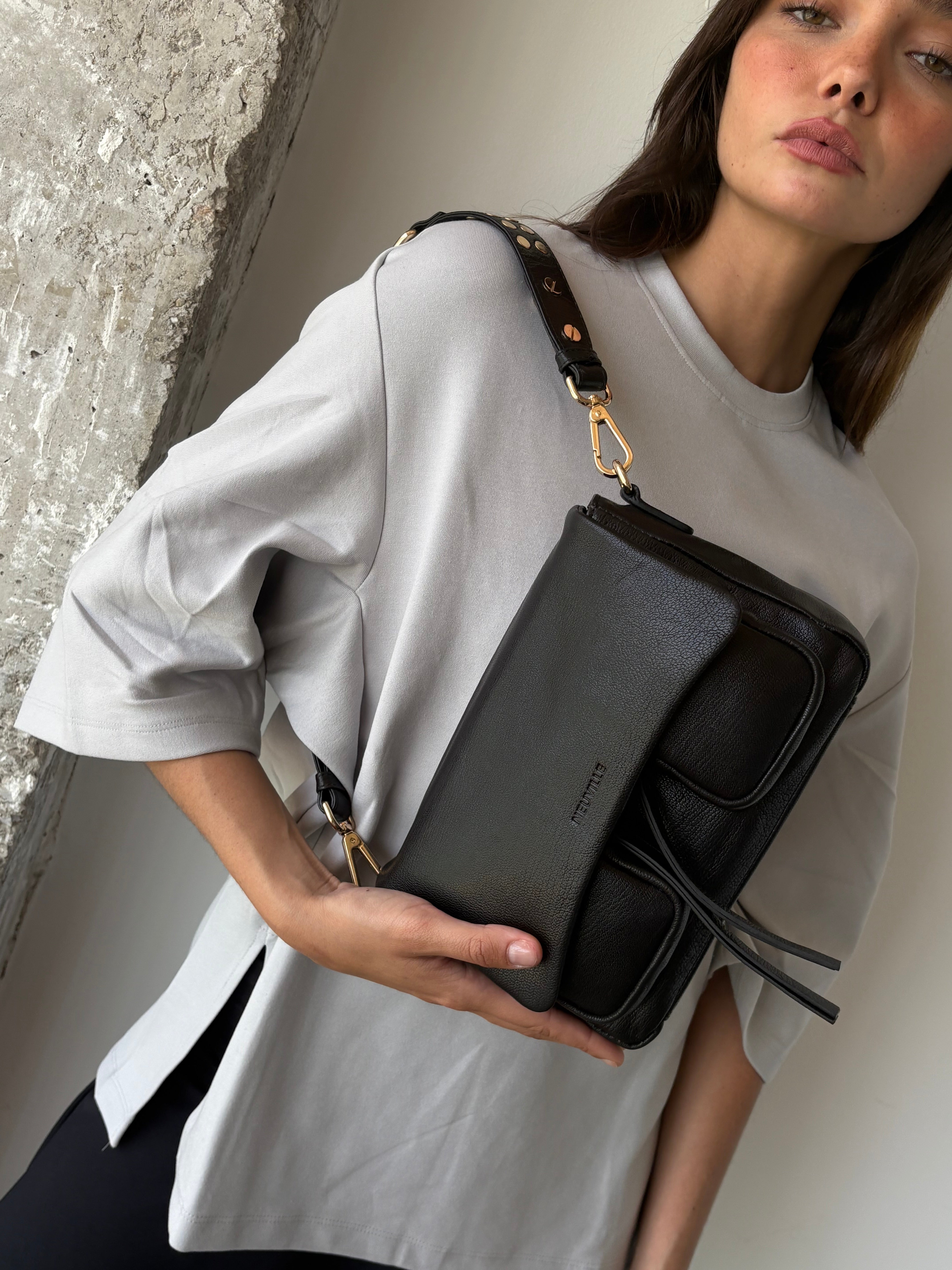 Woman holding a black handbag with a visible brand logo.