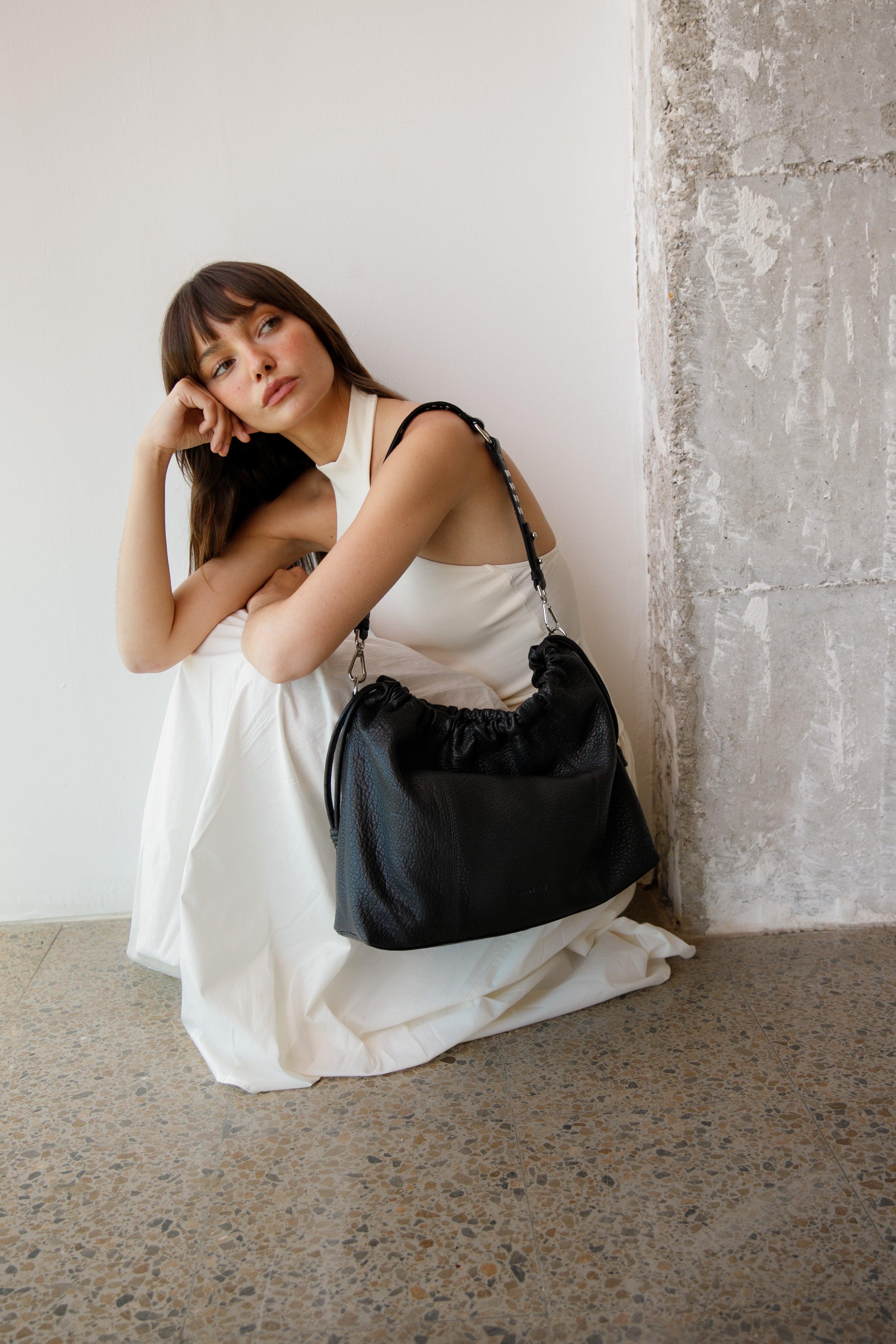 Woman holding a black Elliot Neuville handbag against a white wall.