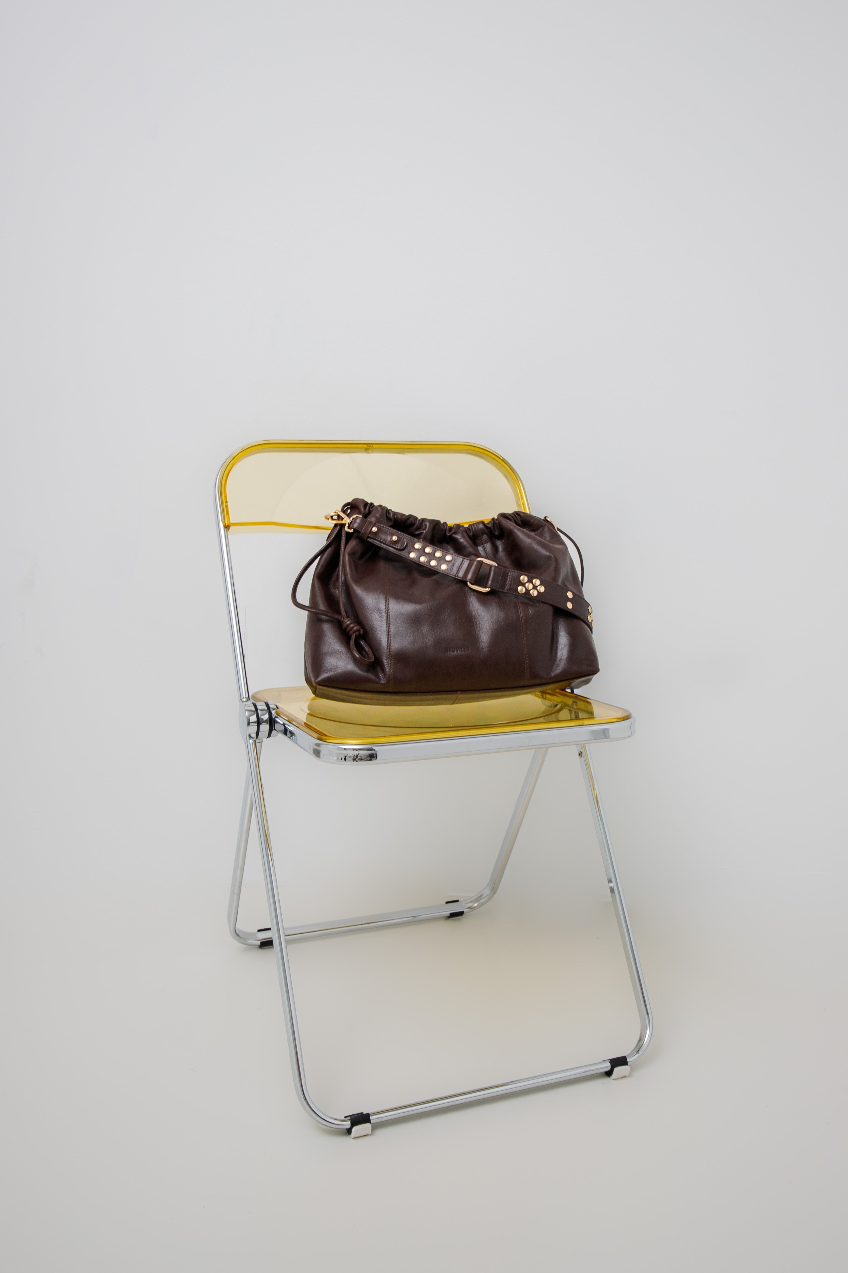 Elliot Chocolate (gold) Brown  leather handbag on a yellow folding chair against a white background