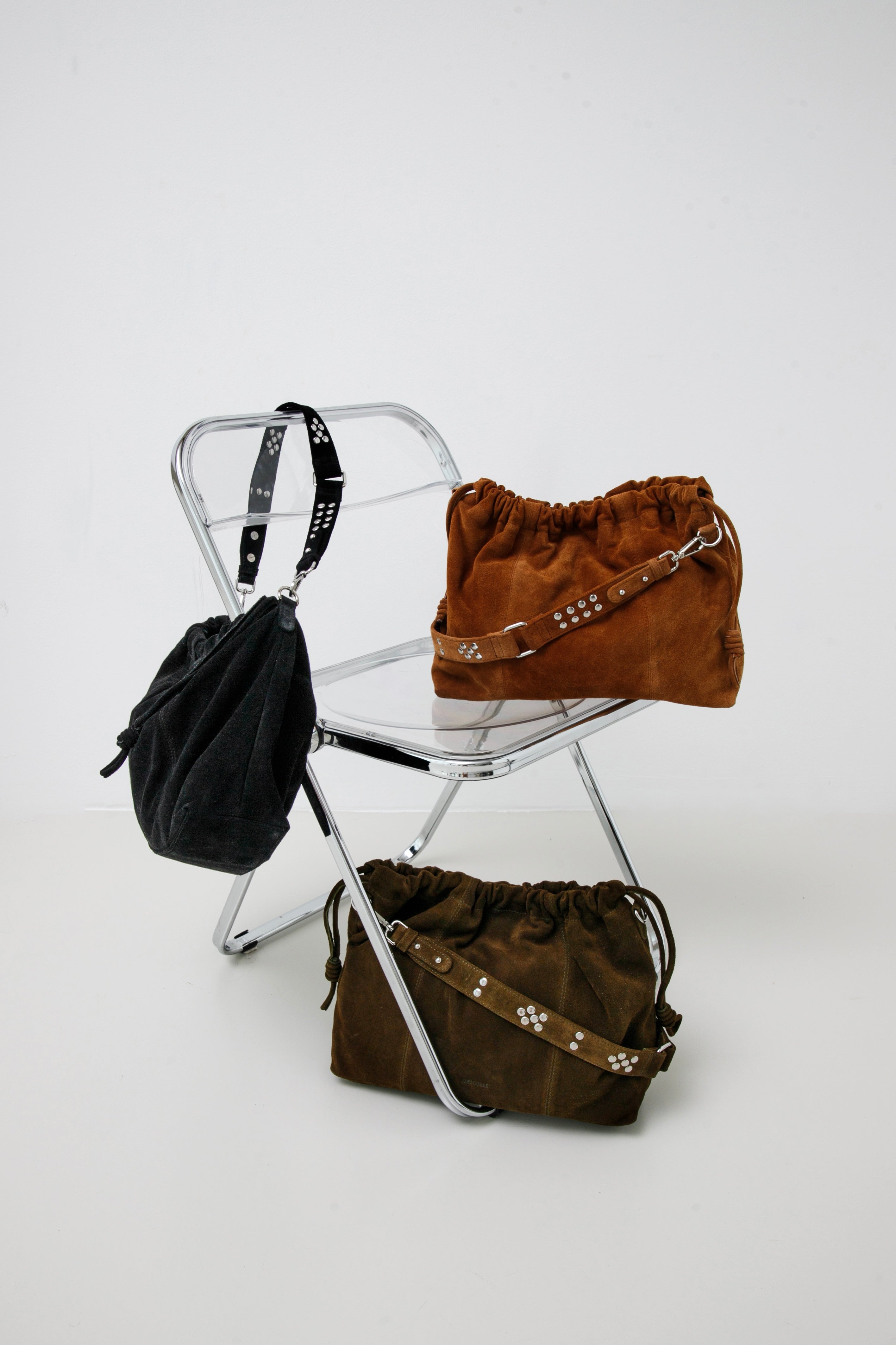 Elliot Black suede, Elliot Caremel suede and Elliot khaki suede bags  on a white chair against a white background: Neuville leather bags.