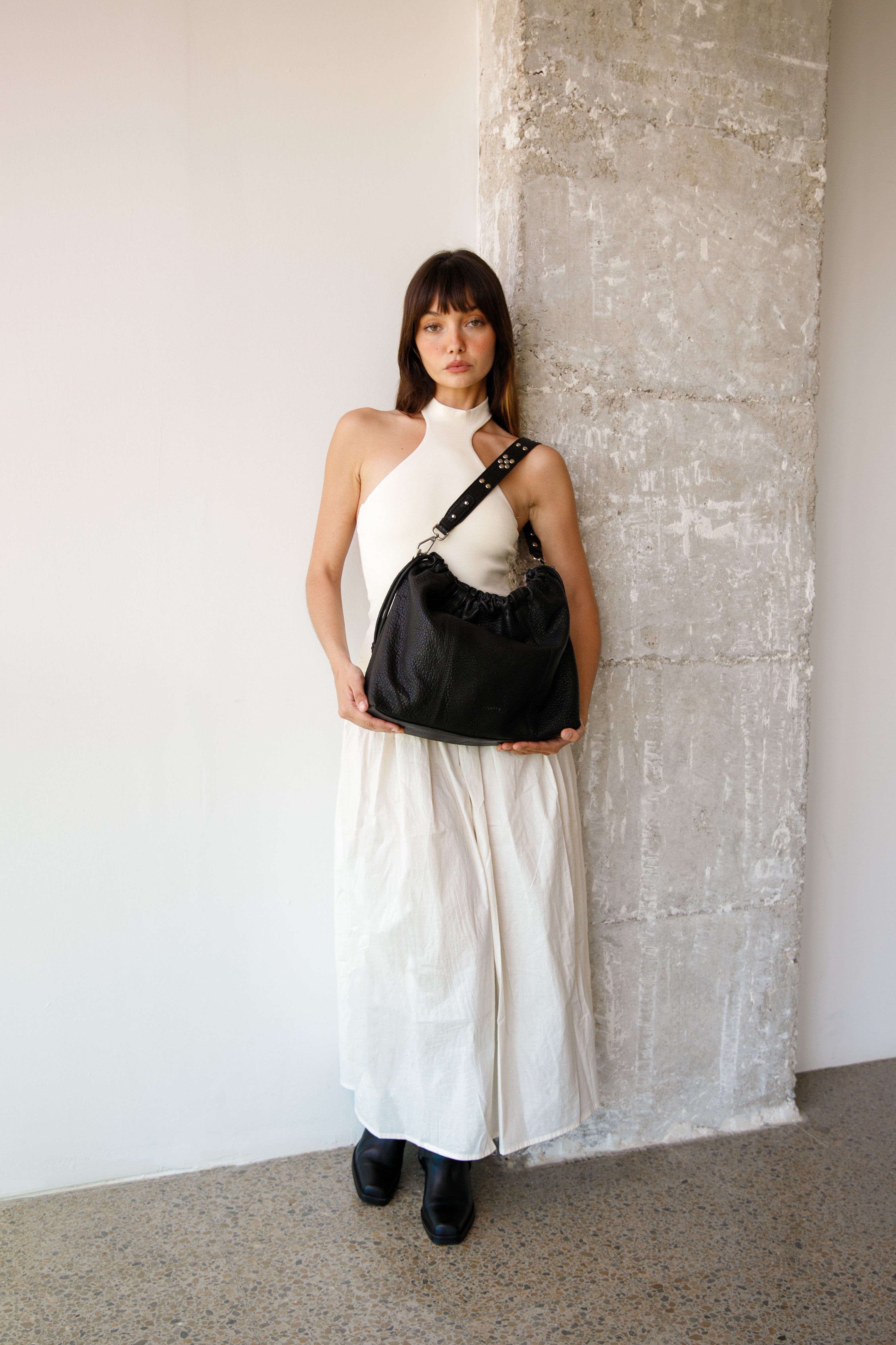 Woman in a white dress holding Bubble black Elliot Neuville bag against a textured wall.