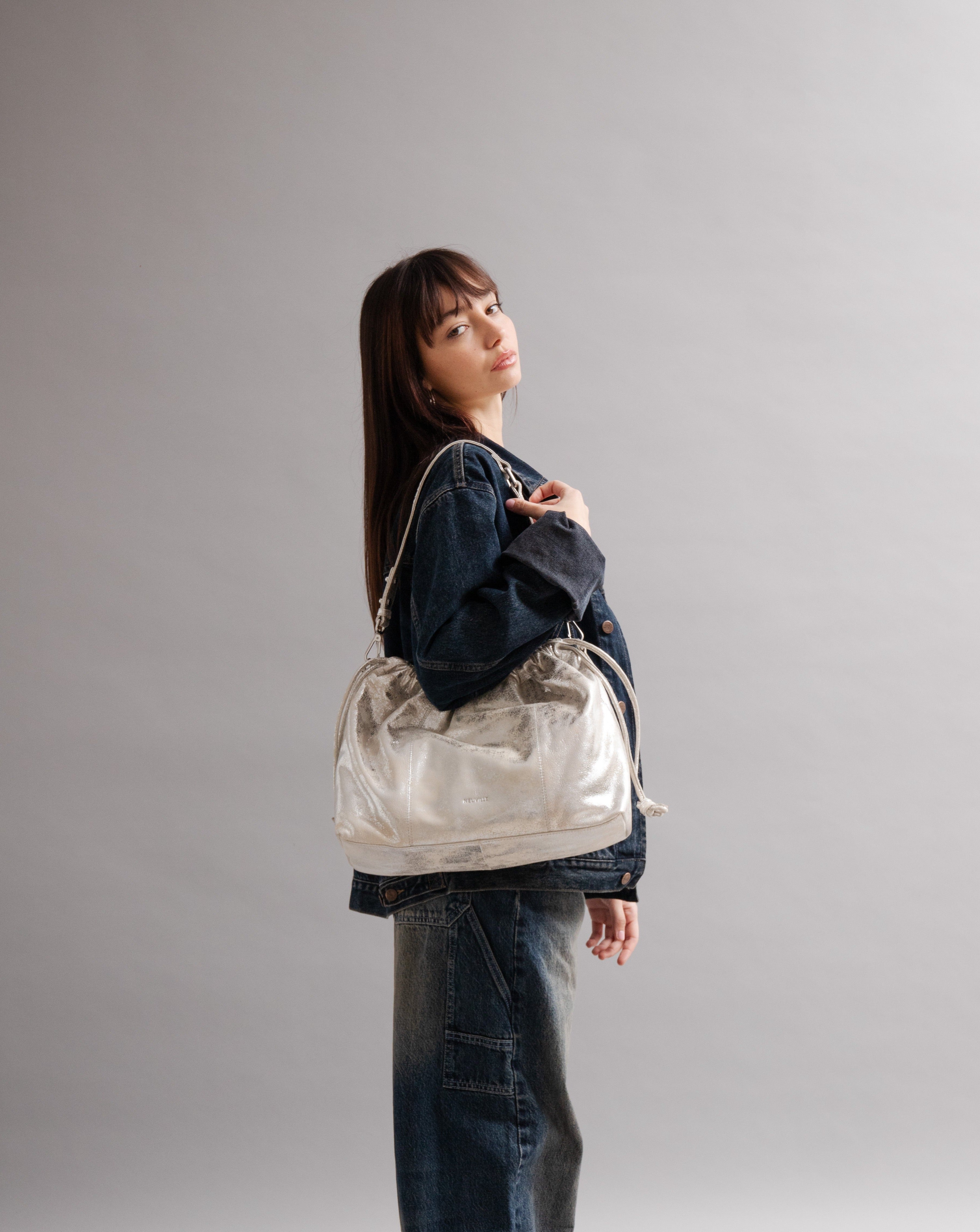 Elliot Sand Gold metallic drawstring bag on a model of in front of a grey background: Neuville bag