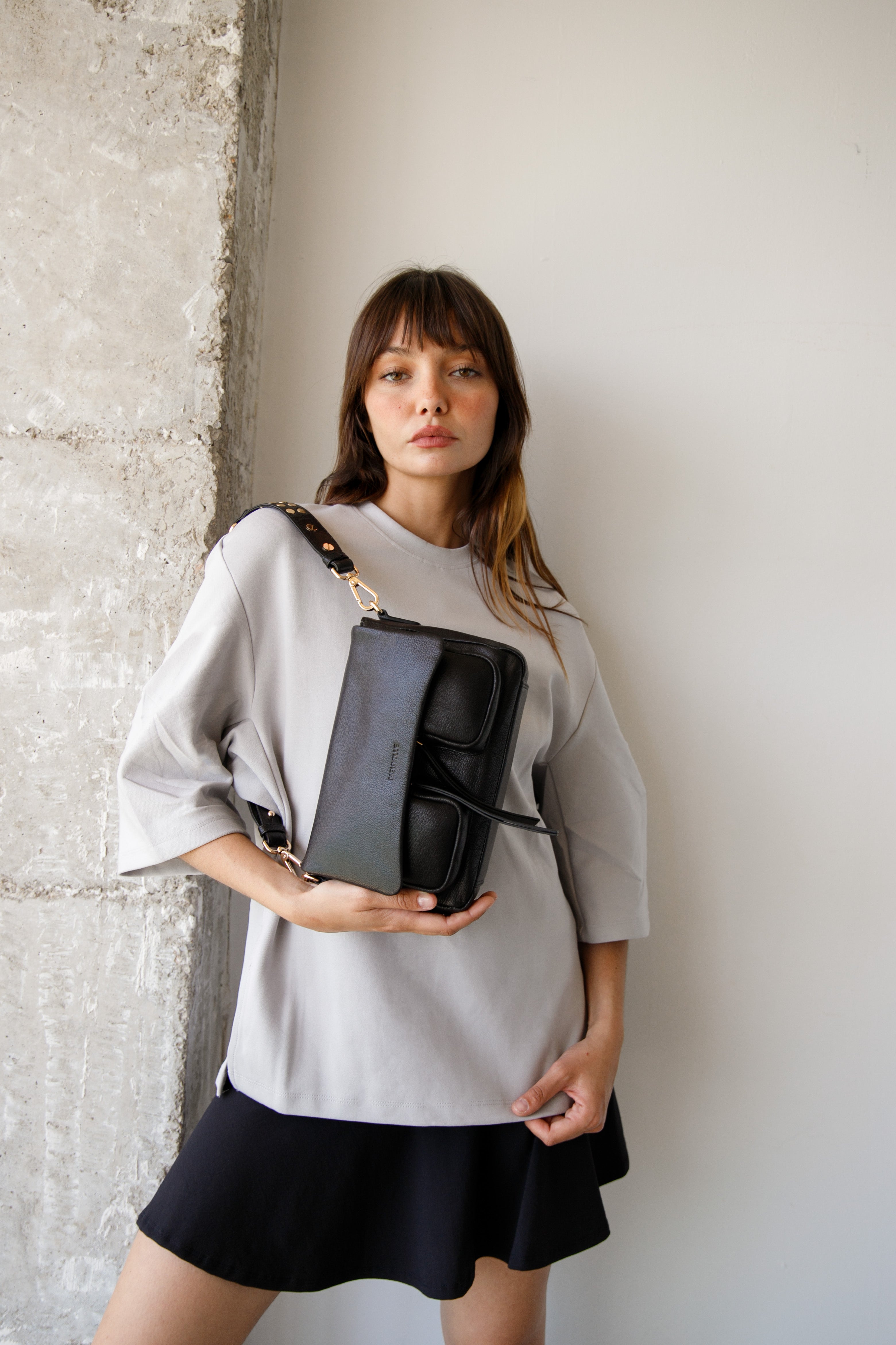 Woman holding a black leather handbag against a neutral background. Maxke Black (gold) Neuville