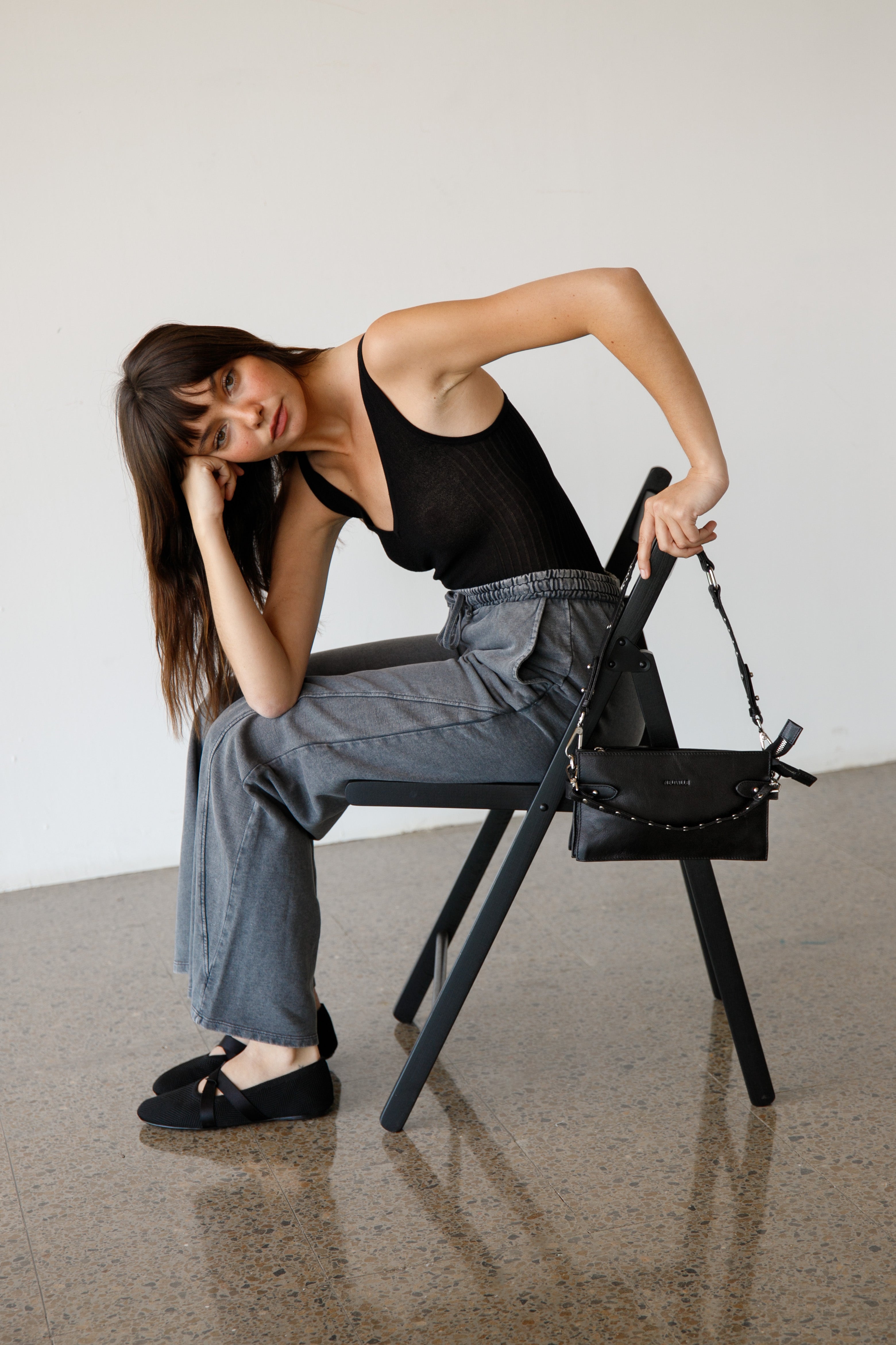 Woman sitting on a chair with a black handbag next to her against a plain background